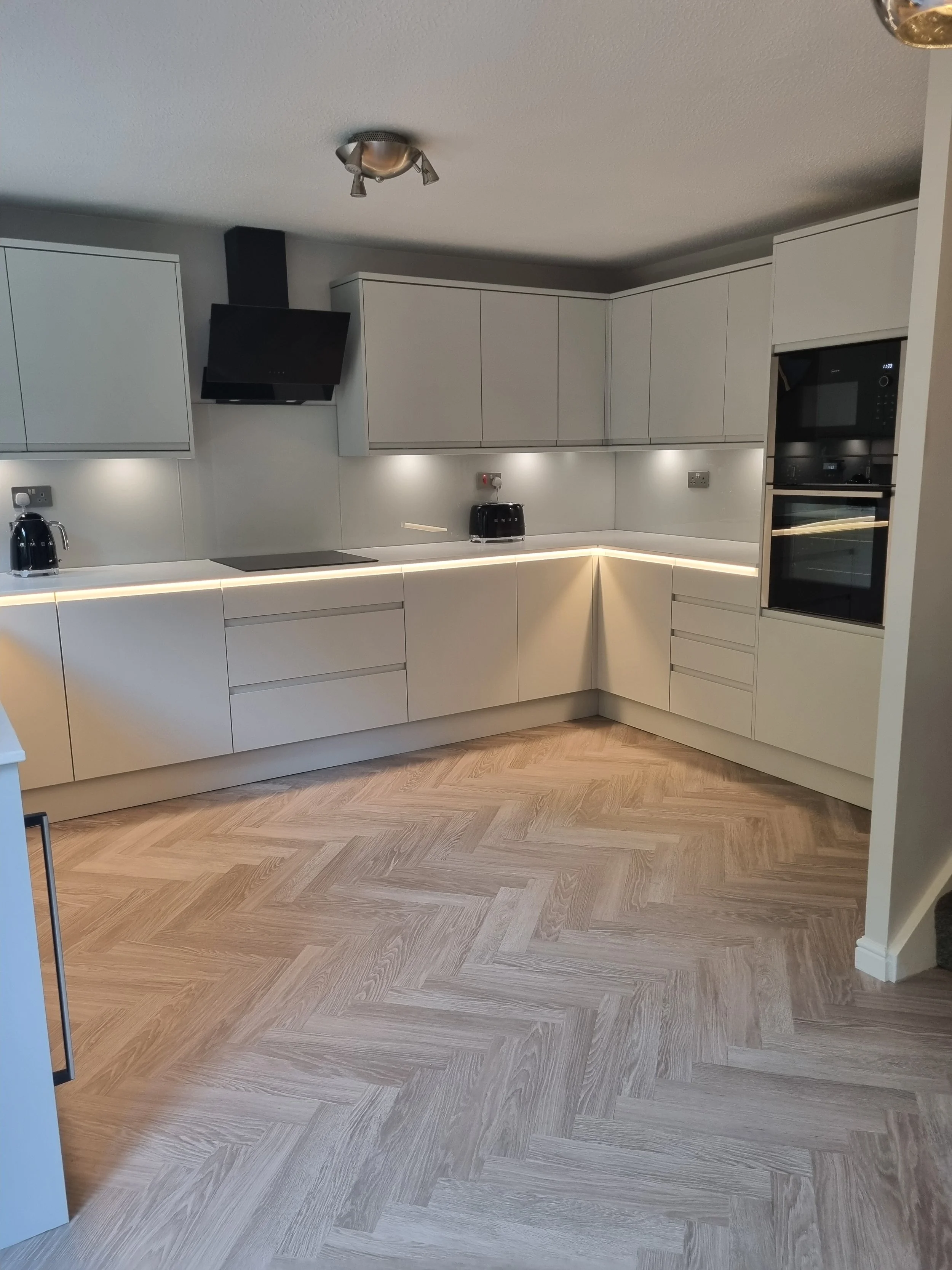 Modern kitchen renovation by Oliver Francis Interiors featuring a stone kitchen suite and worktops with integrated under worktop lighting and light wood flooring