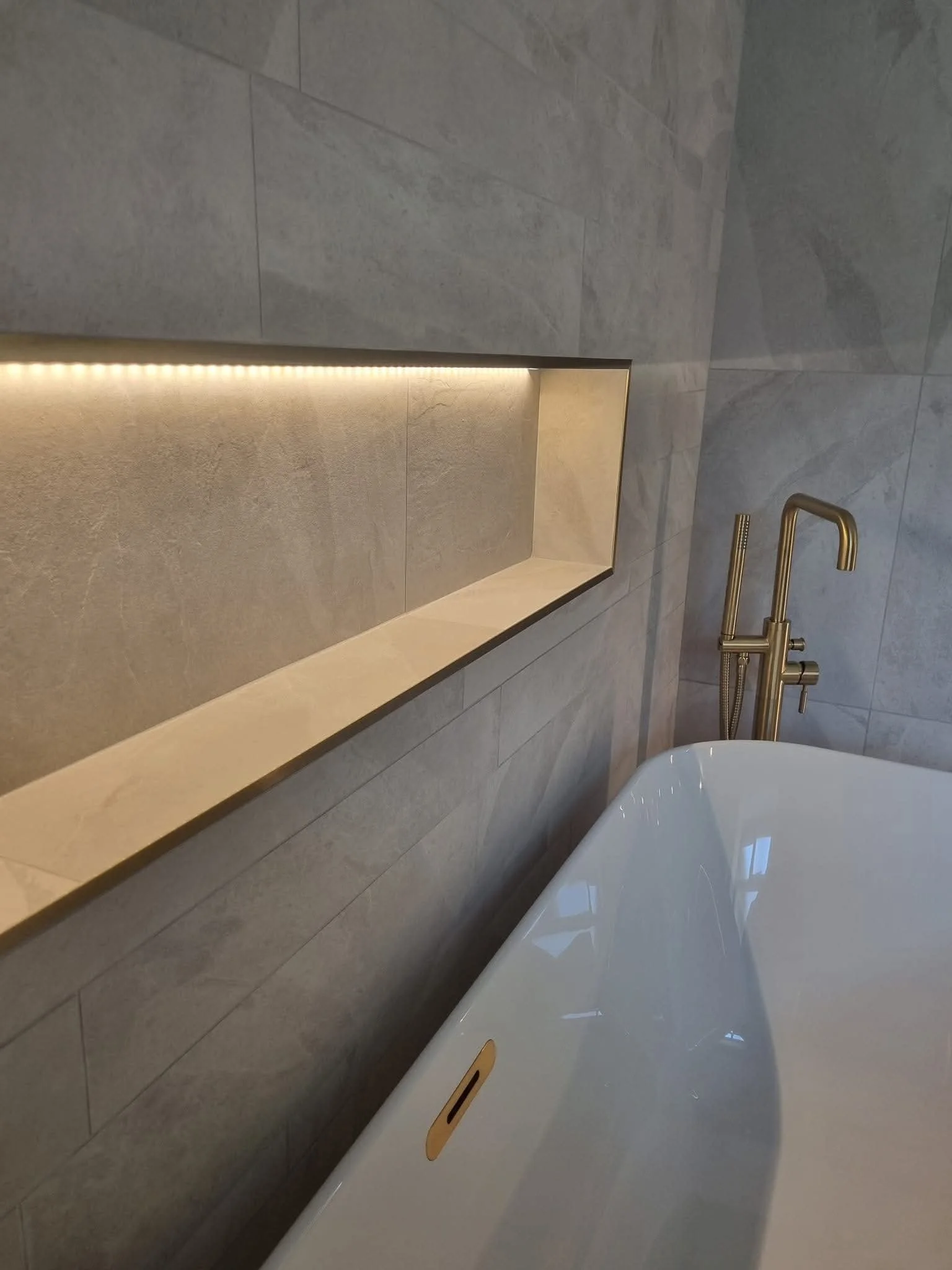 Recessed bathroom wall niche with warm LED lighting above a freestanding bath.