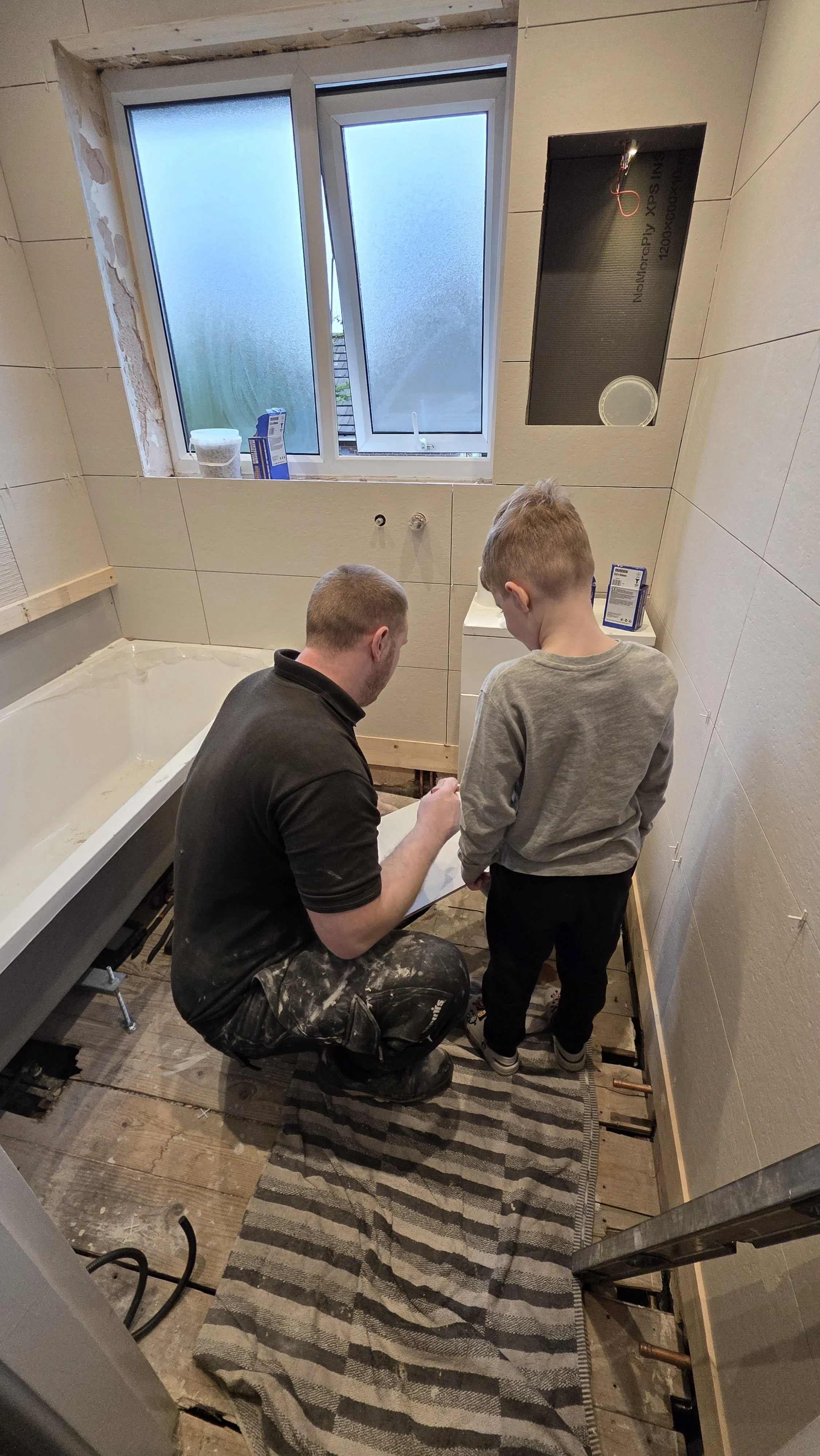 Mike from Oliver Francis Interiors working on a bathroom renovation with his son alongside him.