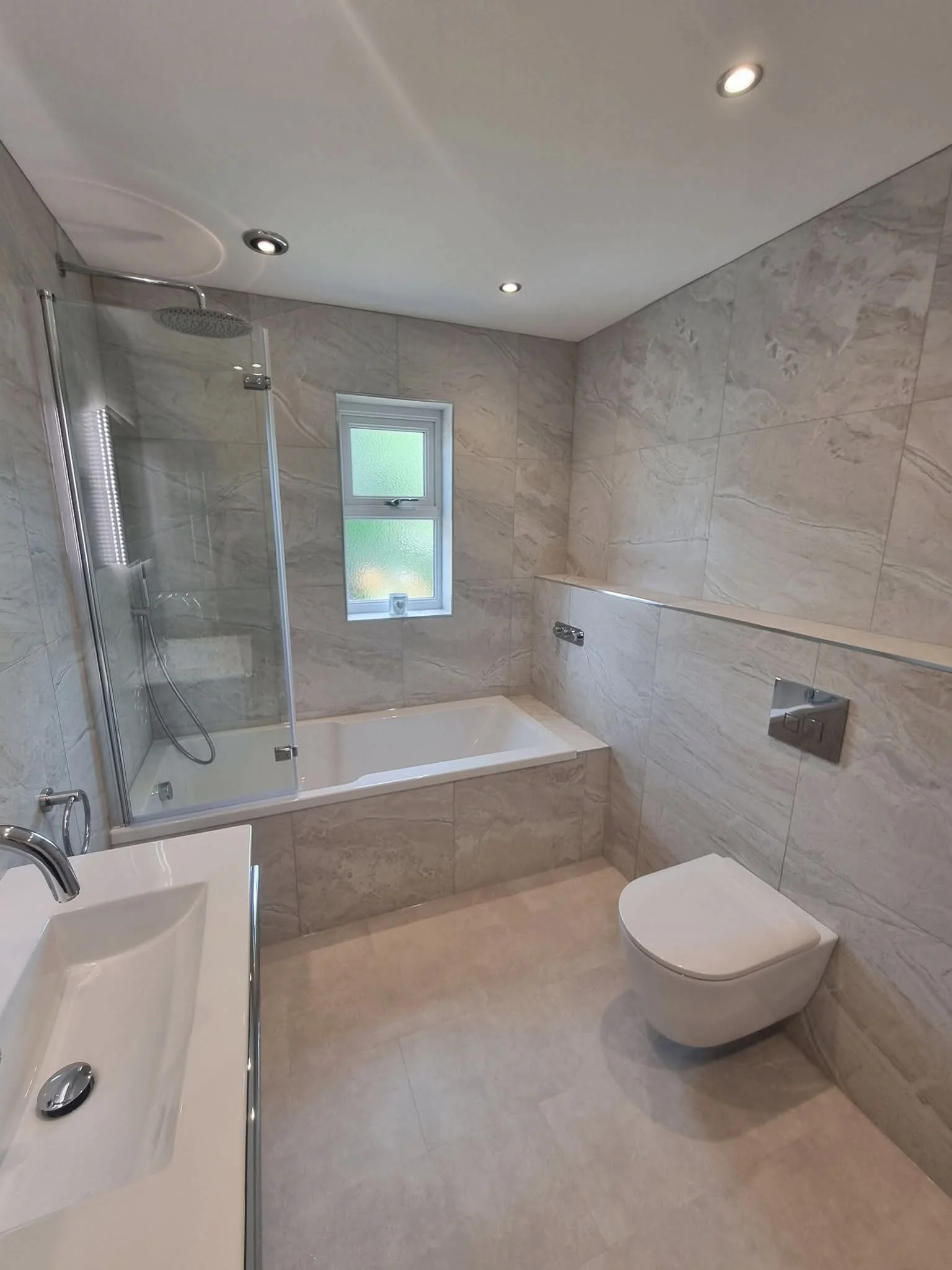 Bathroom renovation in Hayfield, High Peak, featuring a tiled bath and shower, wall-hung toilet and modern vanity unit.