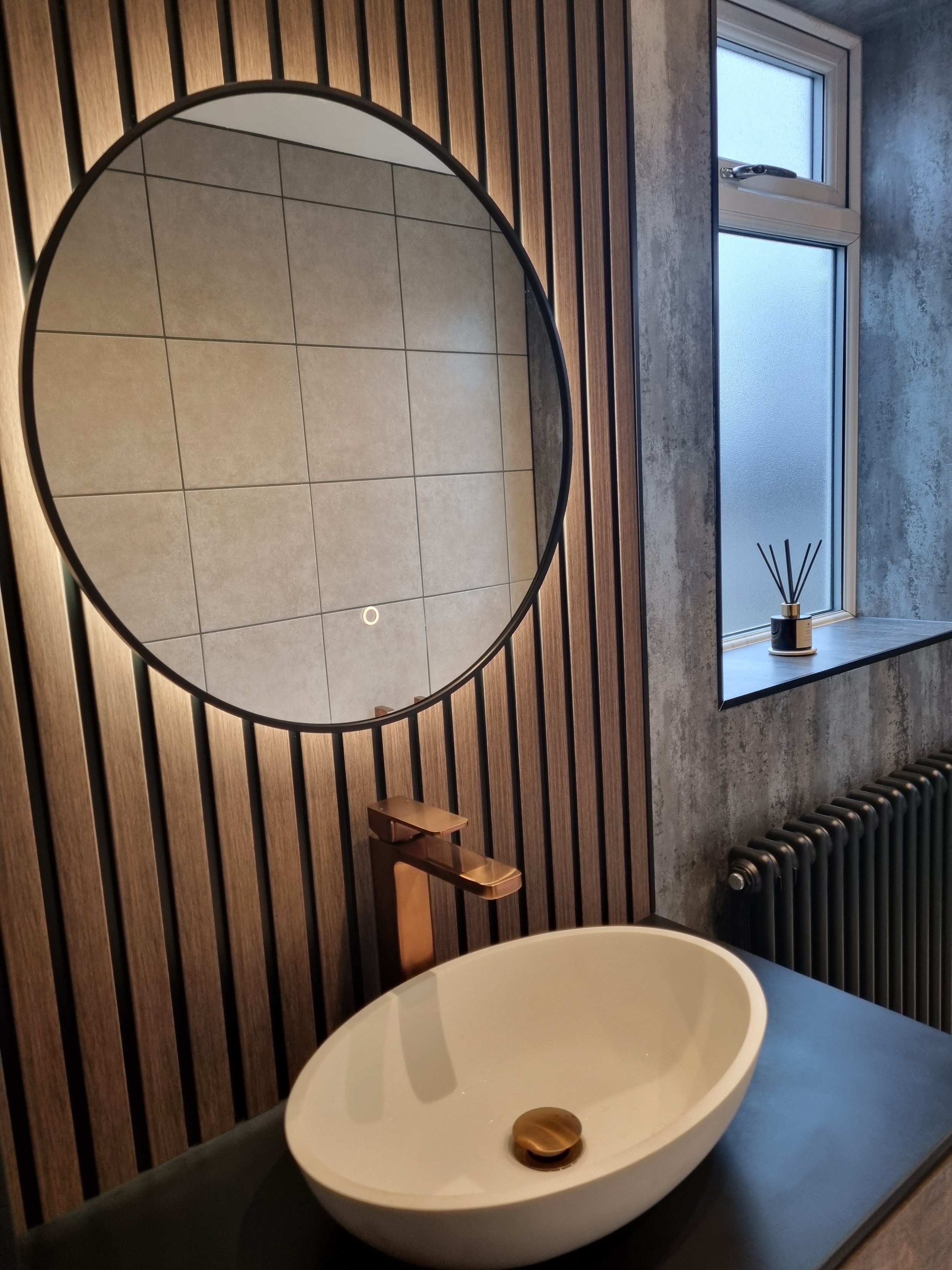 Contemporary bathroom featuring a freestanding bath, vertical wood-effect slat feature wall, round mirror and natural finishing touches.