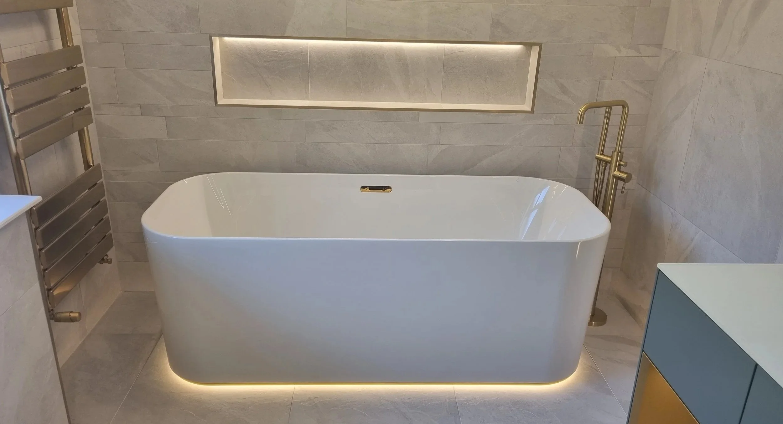 Completed bathroom renovation in Oldham, Manchester by Oliver Francis Interiors, featuring a freestanding bath, tiled walls and illuminated recessed shelf.