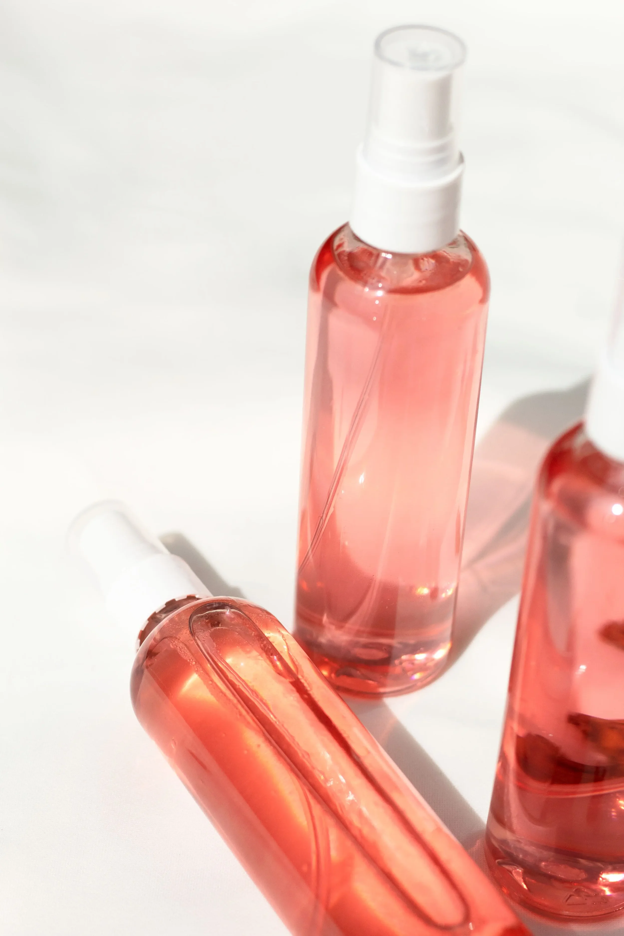 Multiple small glass bottles filled with pink liquid, some with white spray caps, arranged on a white surface.