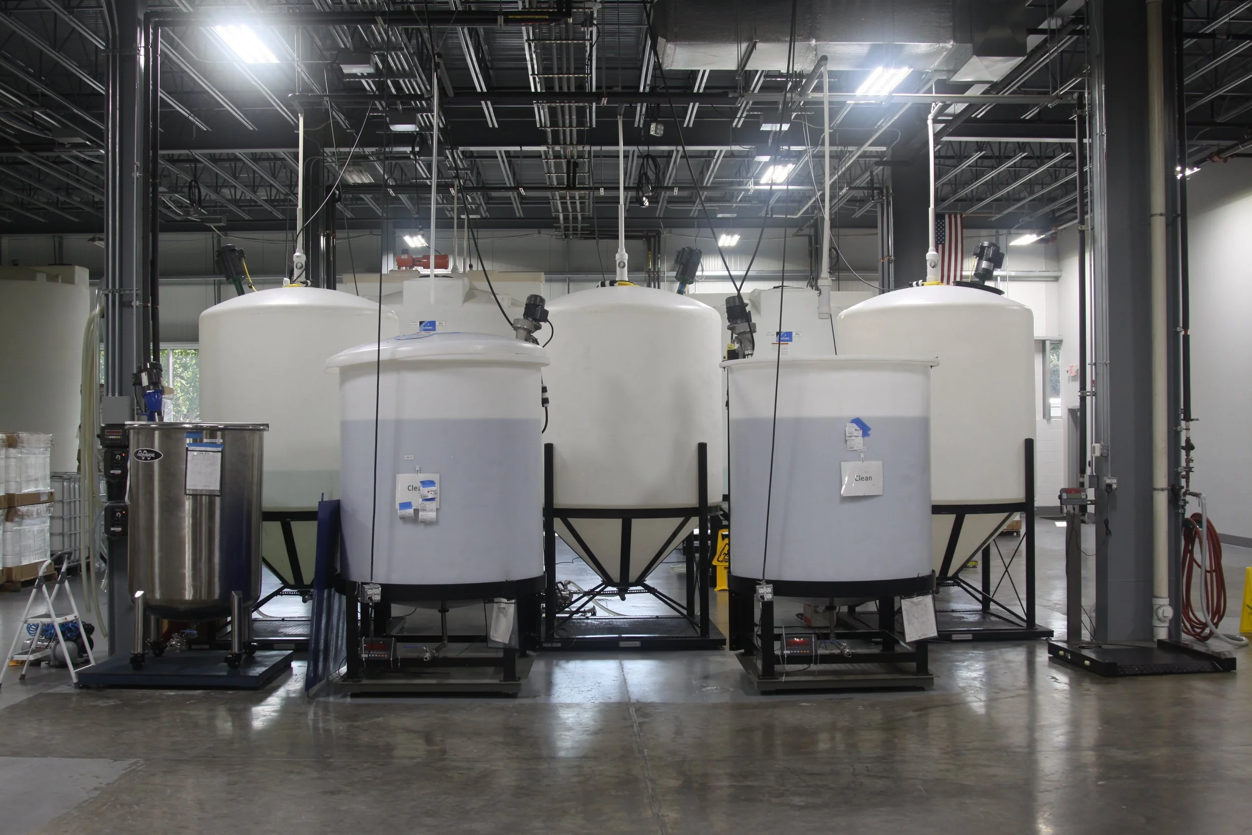 Industrial water treatment or chemical processing tanks and equipment inside a factory or lab with bright overhead lighting.