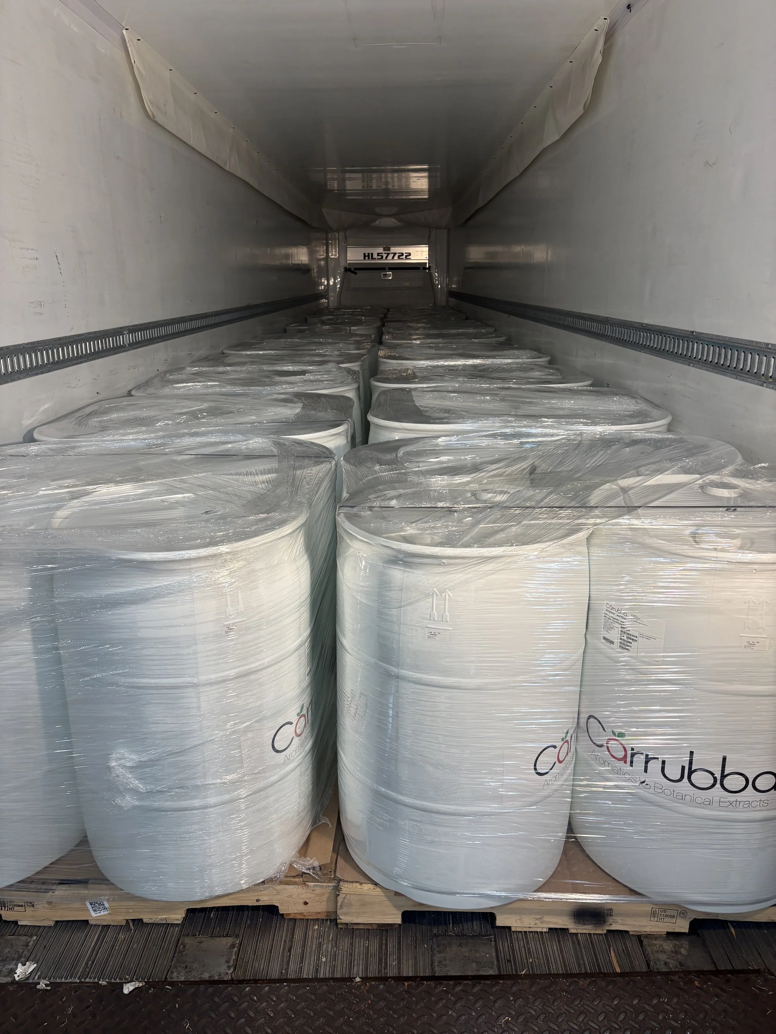 Large cylinders wrapped in plastic and stacked on a wooden pallet inside a truck or warehouse, with the logo 'Cärubba' on the side of the wrapping.