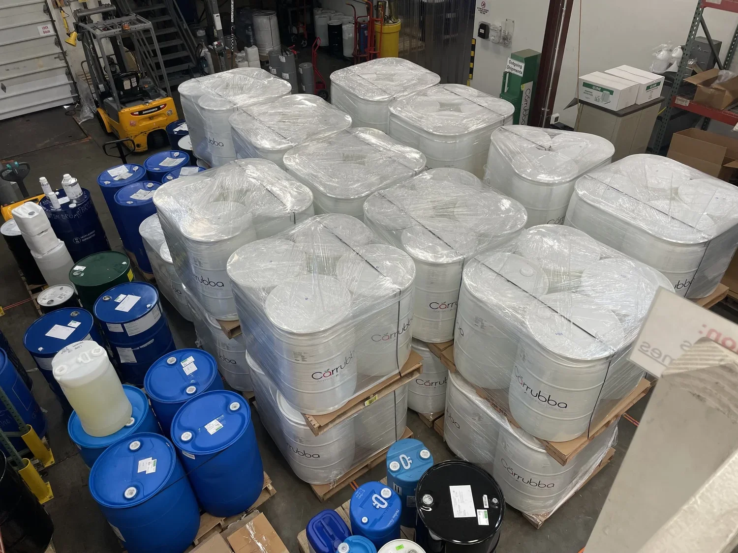 Warehouse with large white and blue barrels, pallets, and shelves containing various items.