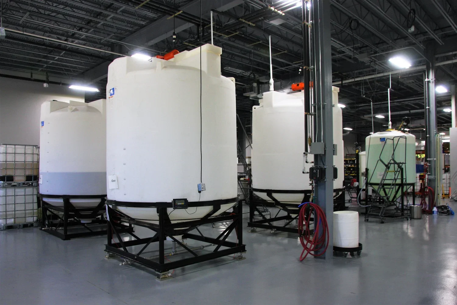 Large white tanks in an industrial setting with black frames, hoses, and other equipment.