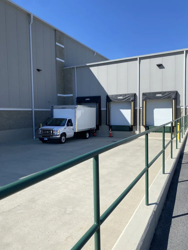 Loading dock with three dock doors, one truck parked near the docks, and a green railing along the ramp.