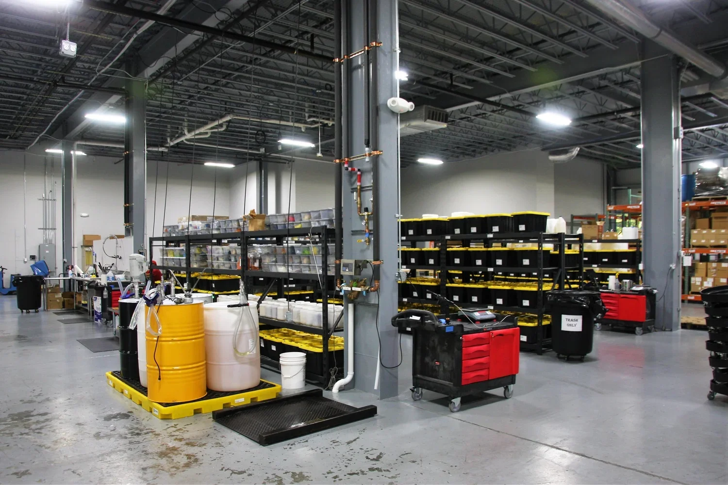 Interior of a warehouse or industrial storage area with shelves of labeled bins, carts, and equipment.