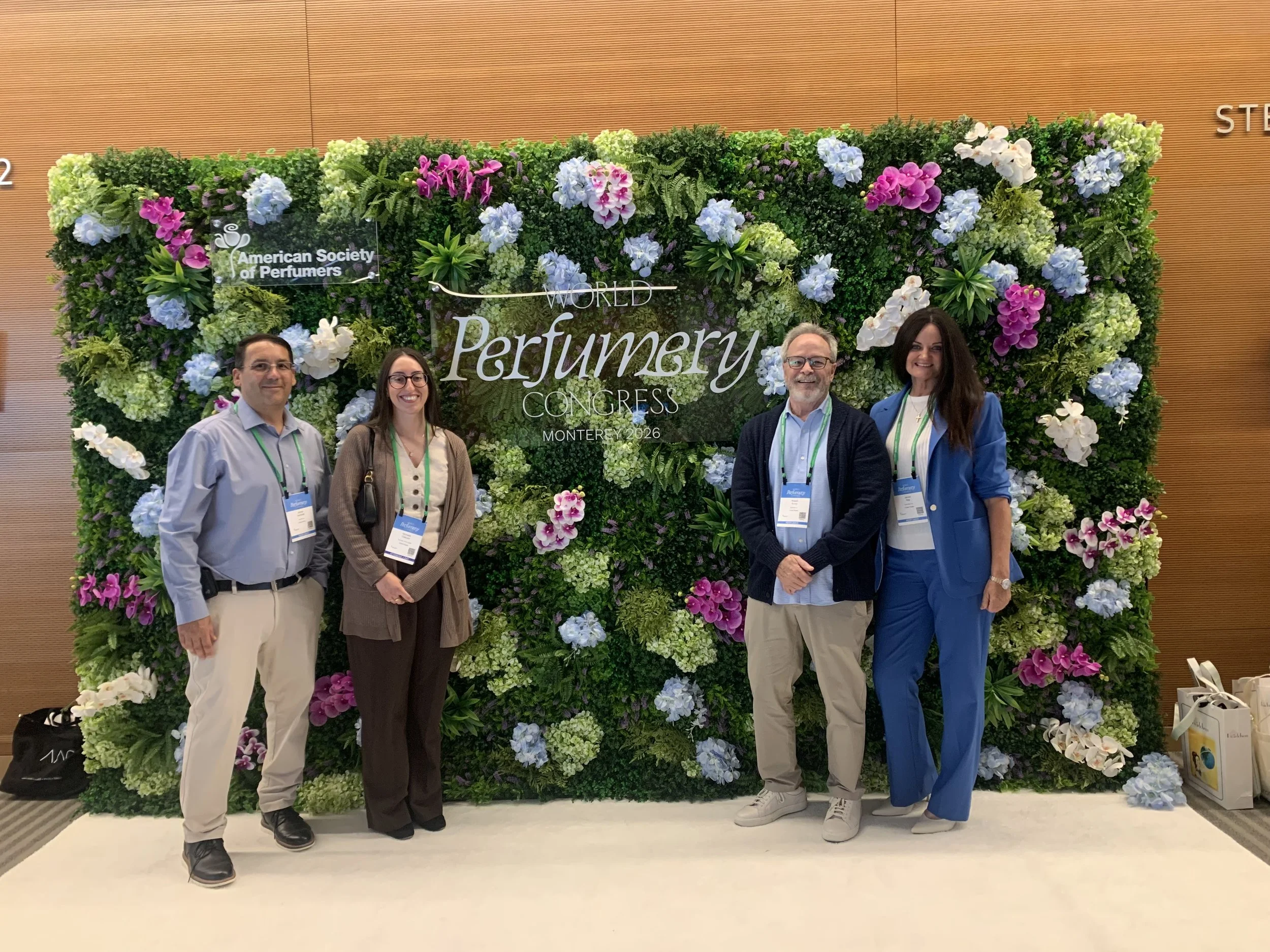 Four people standing in front of a large floral display at the American Society of Perfumer's World Perfumer's Congress in Monterey, 2026.