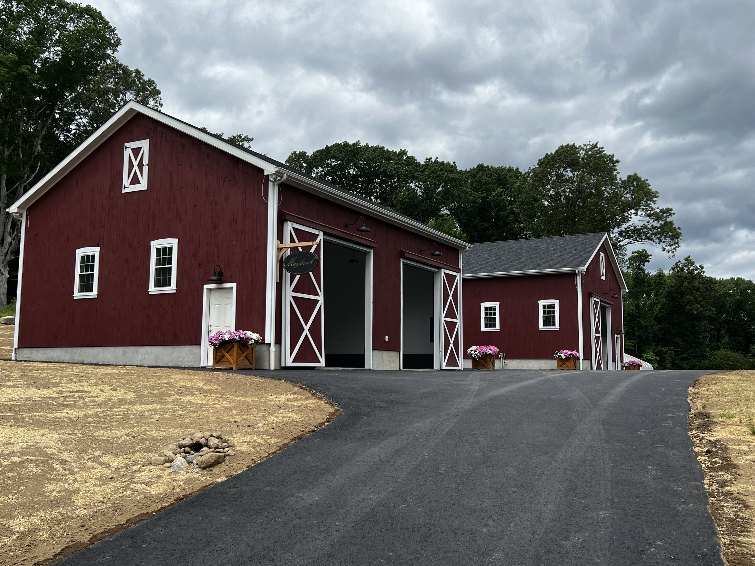 A red barn with white trim, sliding barn doors, and small white-paned windows, set against a backdrop of green trees and a cloudy sky.