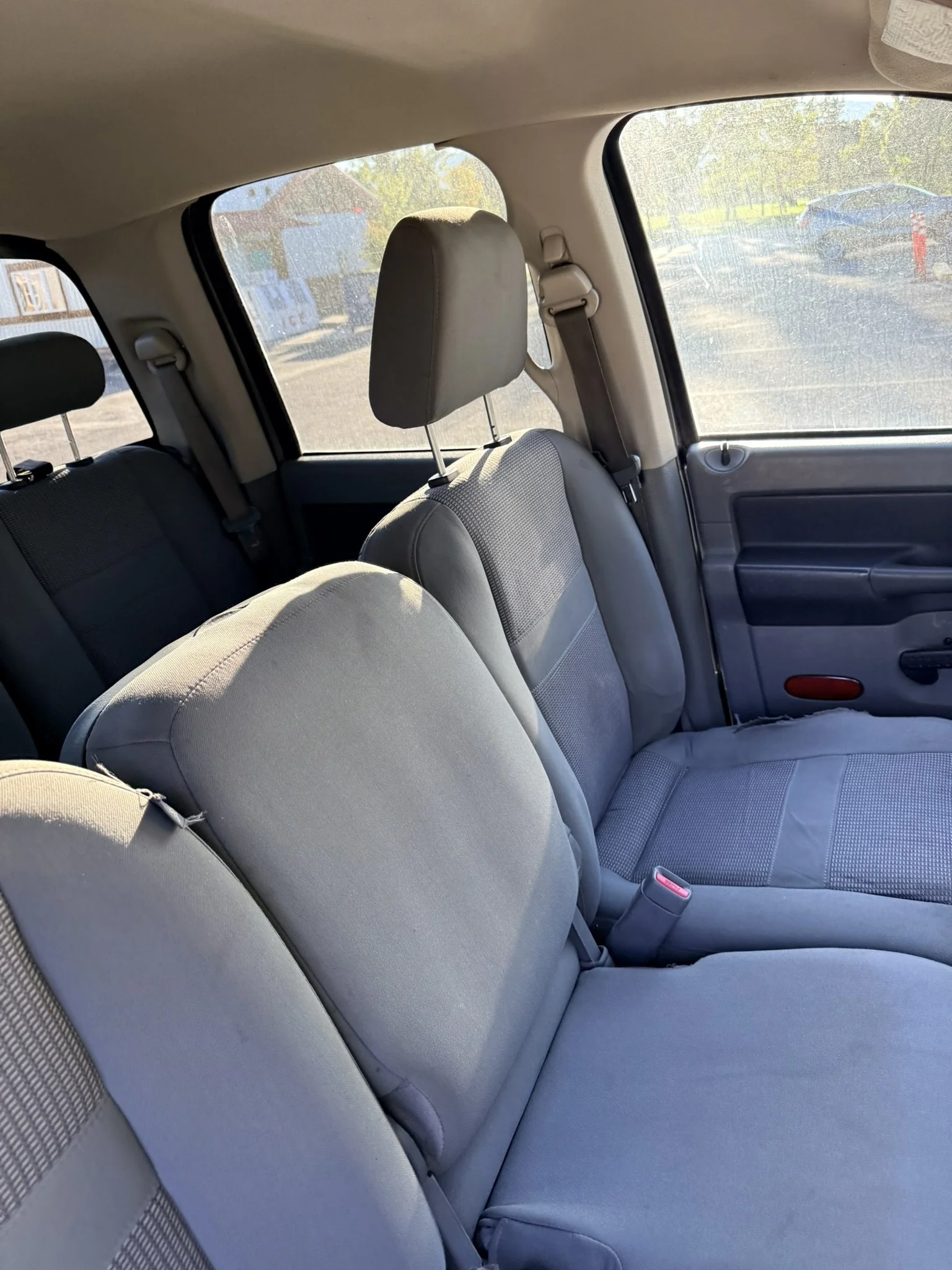 Interior of a car showing the back seats, headrests, and windows with a view of a parking lot and houses outside.