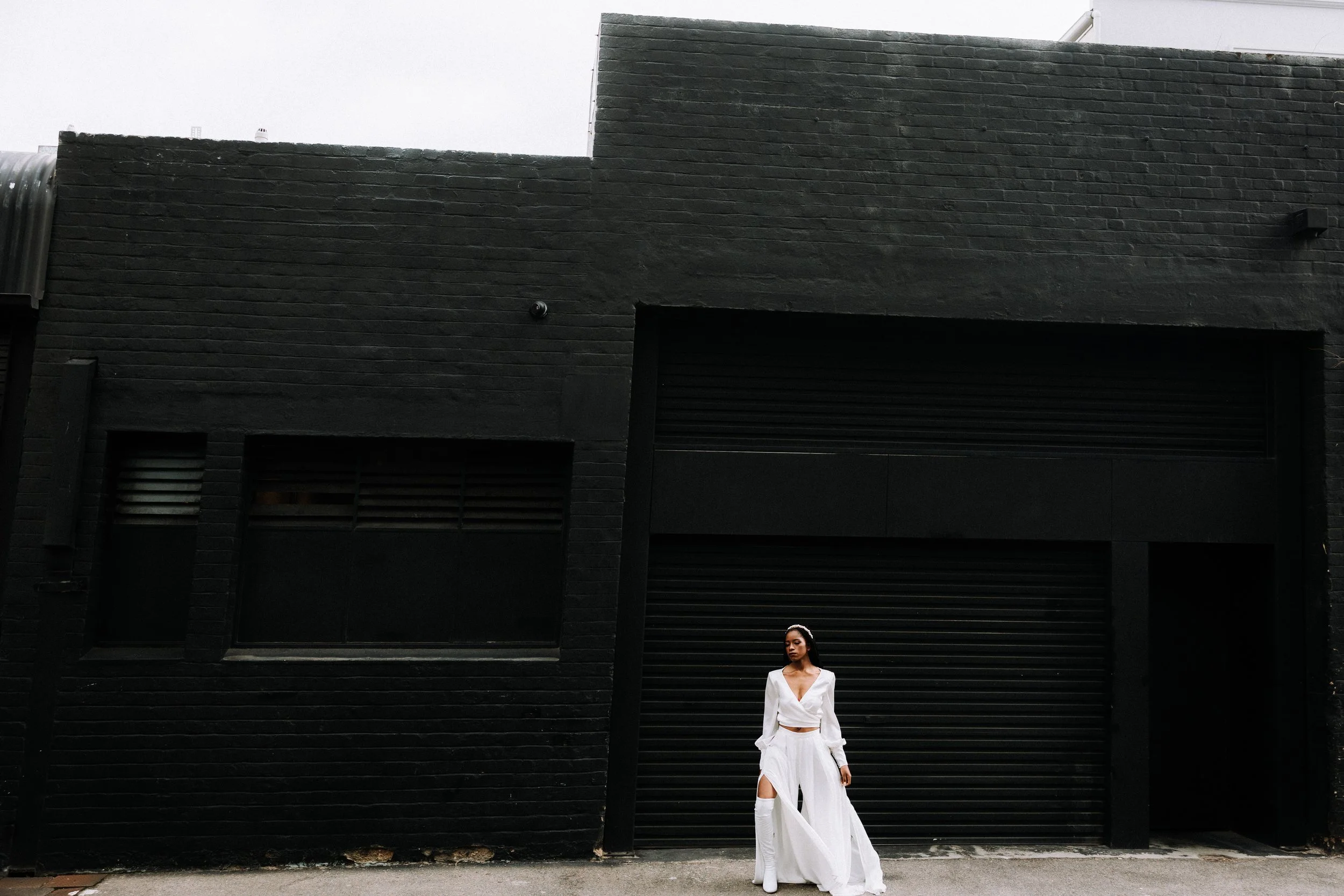 A woman wearing a white outfit standing in front of a large black building with a geometric facade.