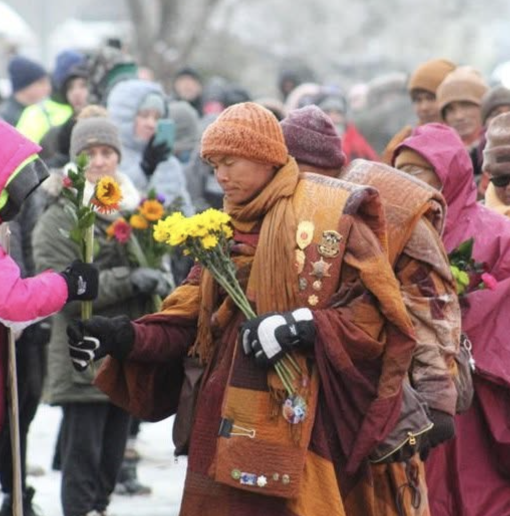 People dressed in warm clothing holding flowers during a gathering or memorial event.