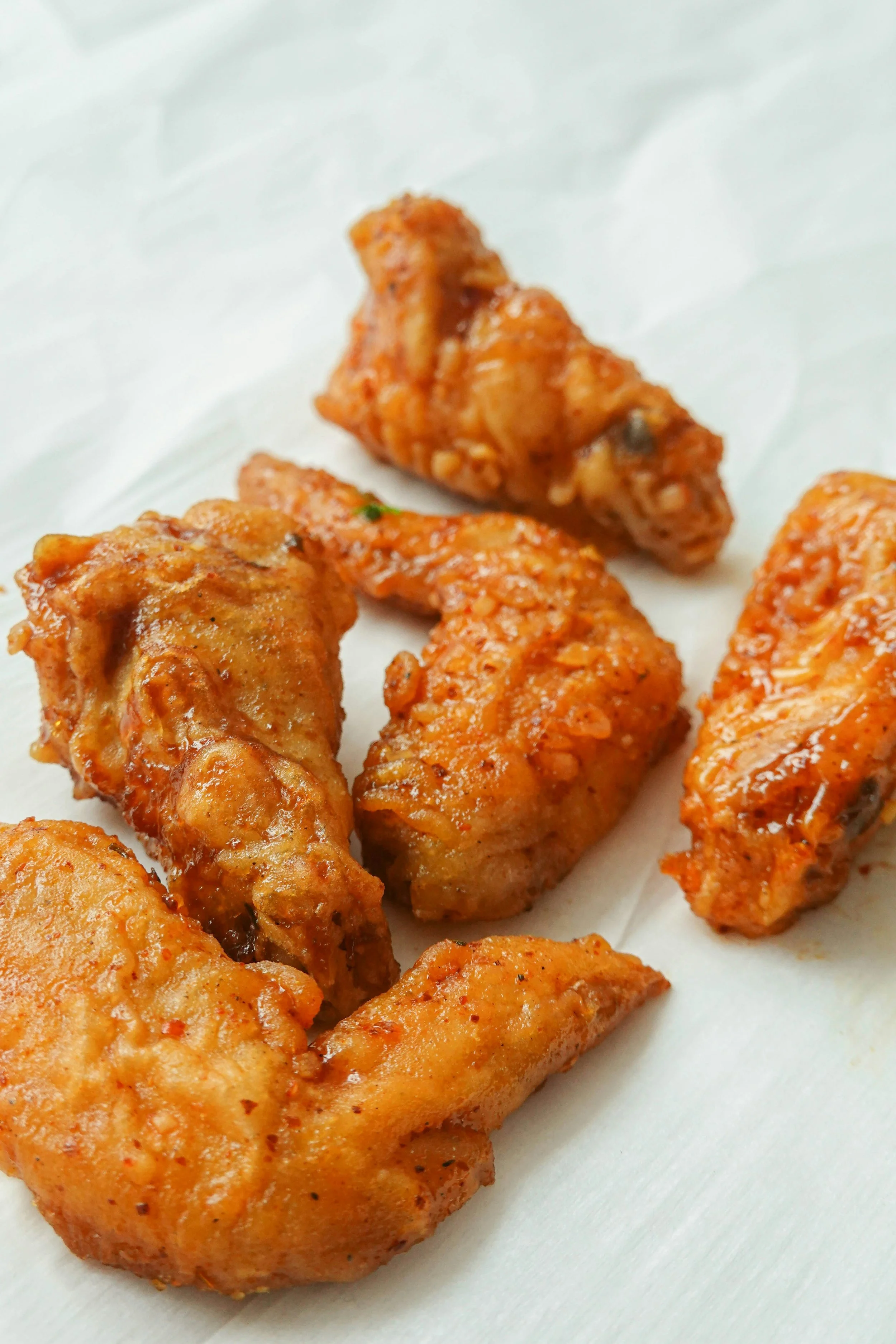 Close-up of several pieces of fried chicken wings on white paper.