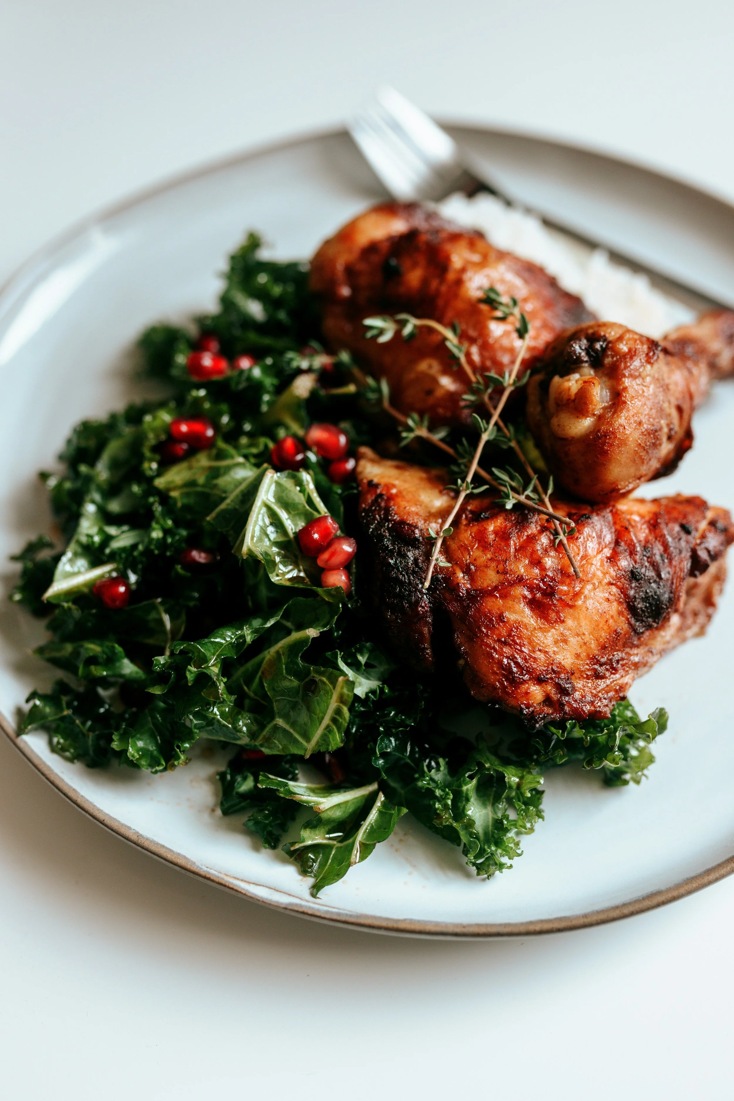 Roasted chicken leg quarter on a white plate with roasted vegetables and fresh herbs