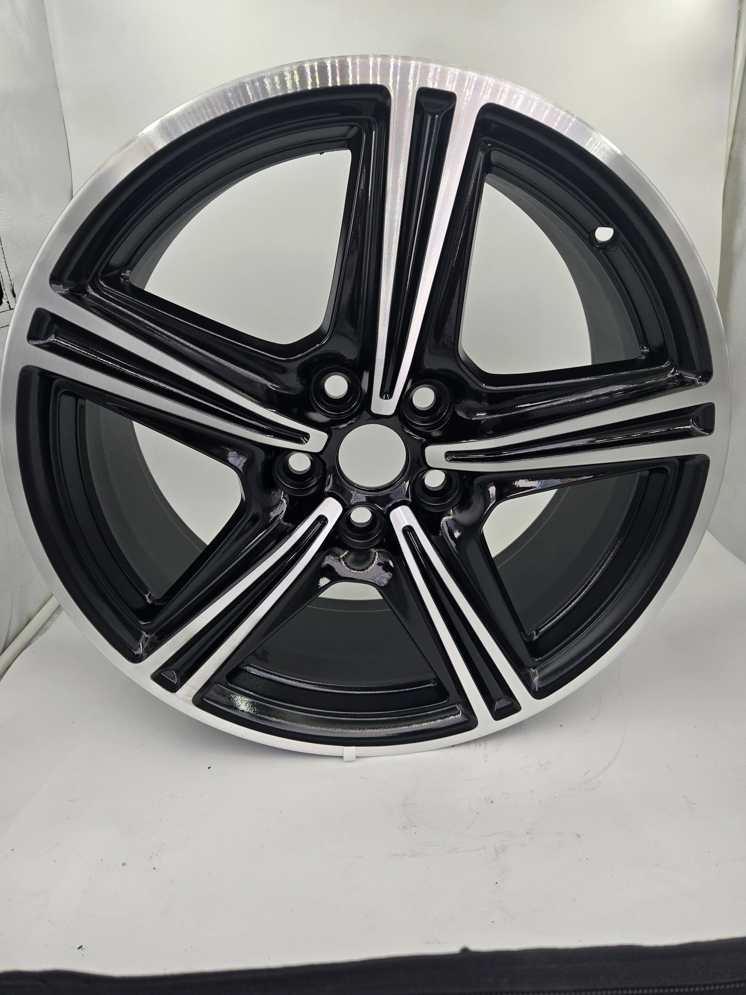 A large, round, metallic car wheel rim with black accents, placed on a white surface against a light-colored background.
