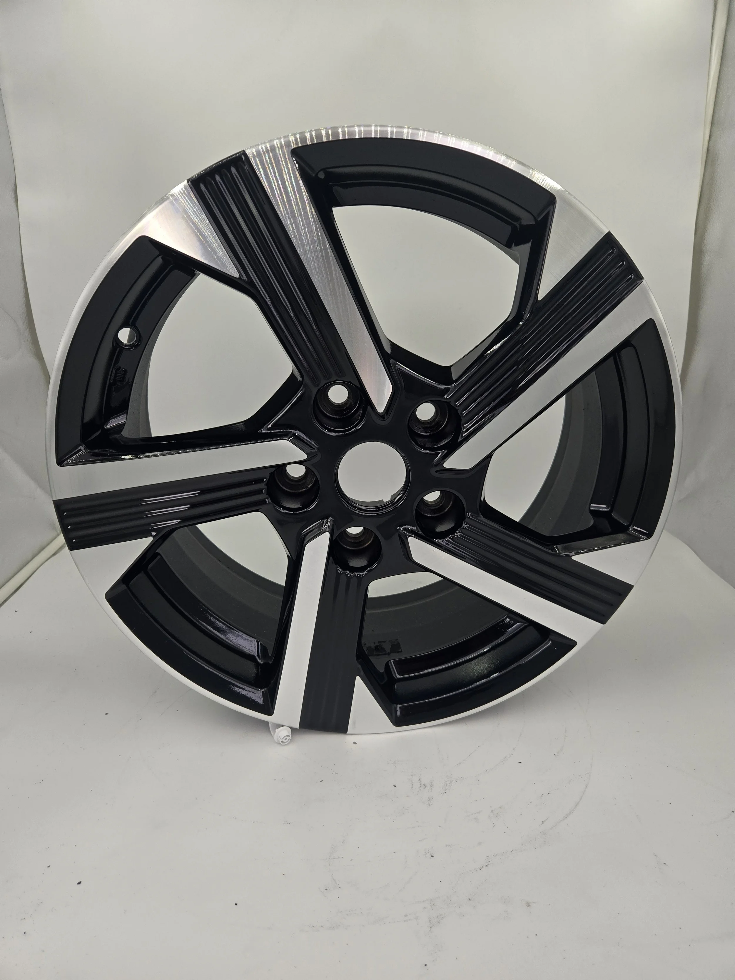 A black and silver alloy wheel rim with a modern, angular design, resting on a white surface.