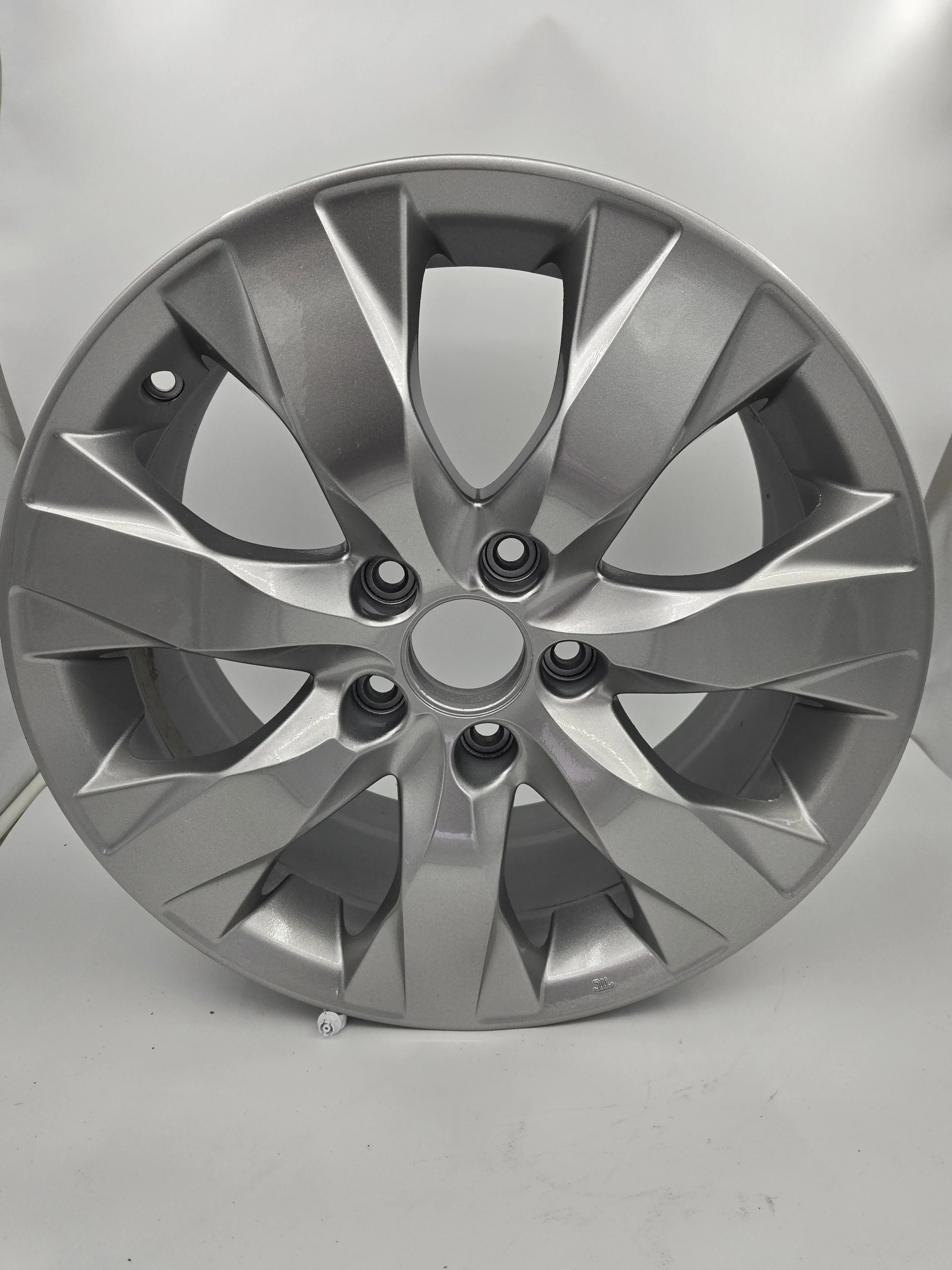 A silver alloy wheel rim for a vehicle, with a multi-spoke design and five lug nut holes, set against a plain light-colored background.