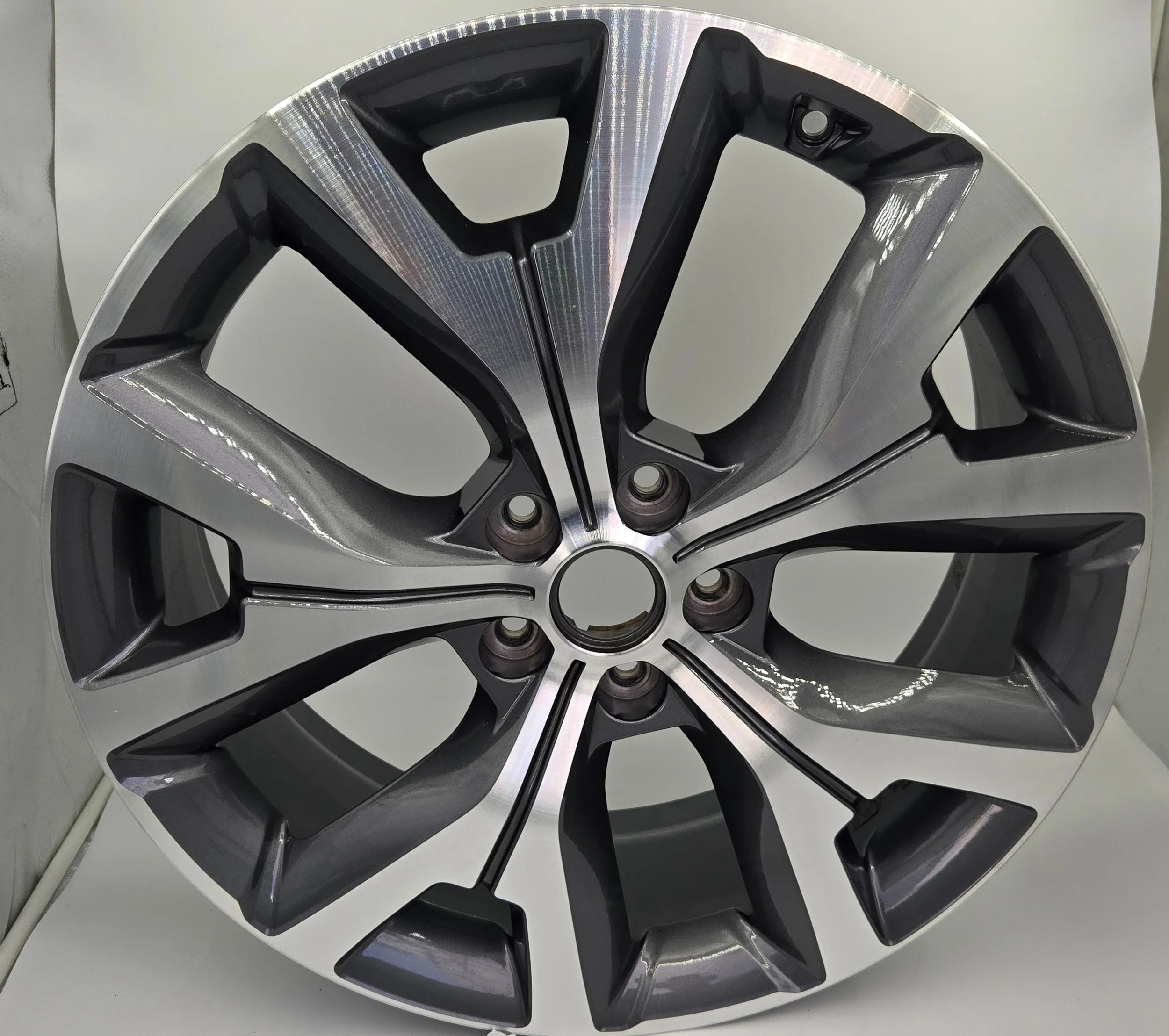 Close-up of a modern metallic multi-spoke car wheel rim with black accents, displayed on a white surface.
