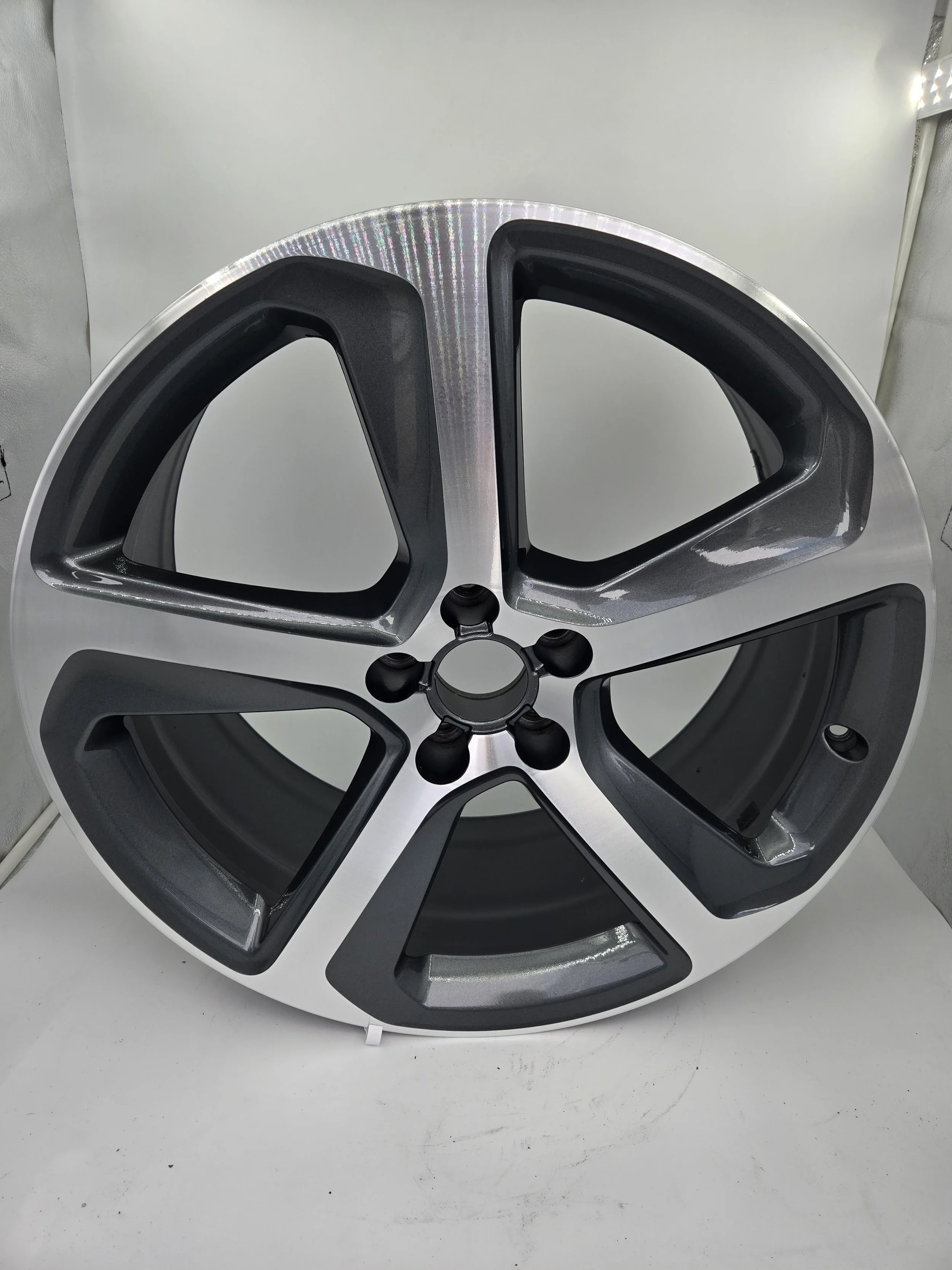 A set of five car wheel rims stacked on top of each other, with the top rim showing a shiny silver outer edge and black inner section, placed on a white surface.