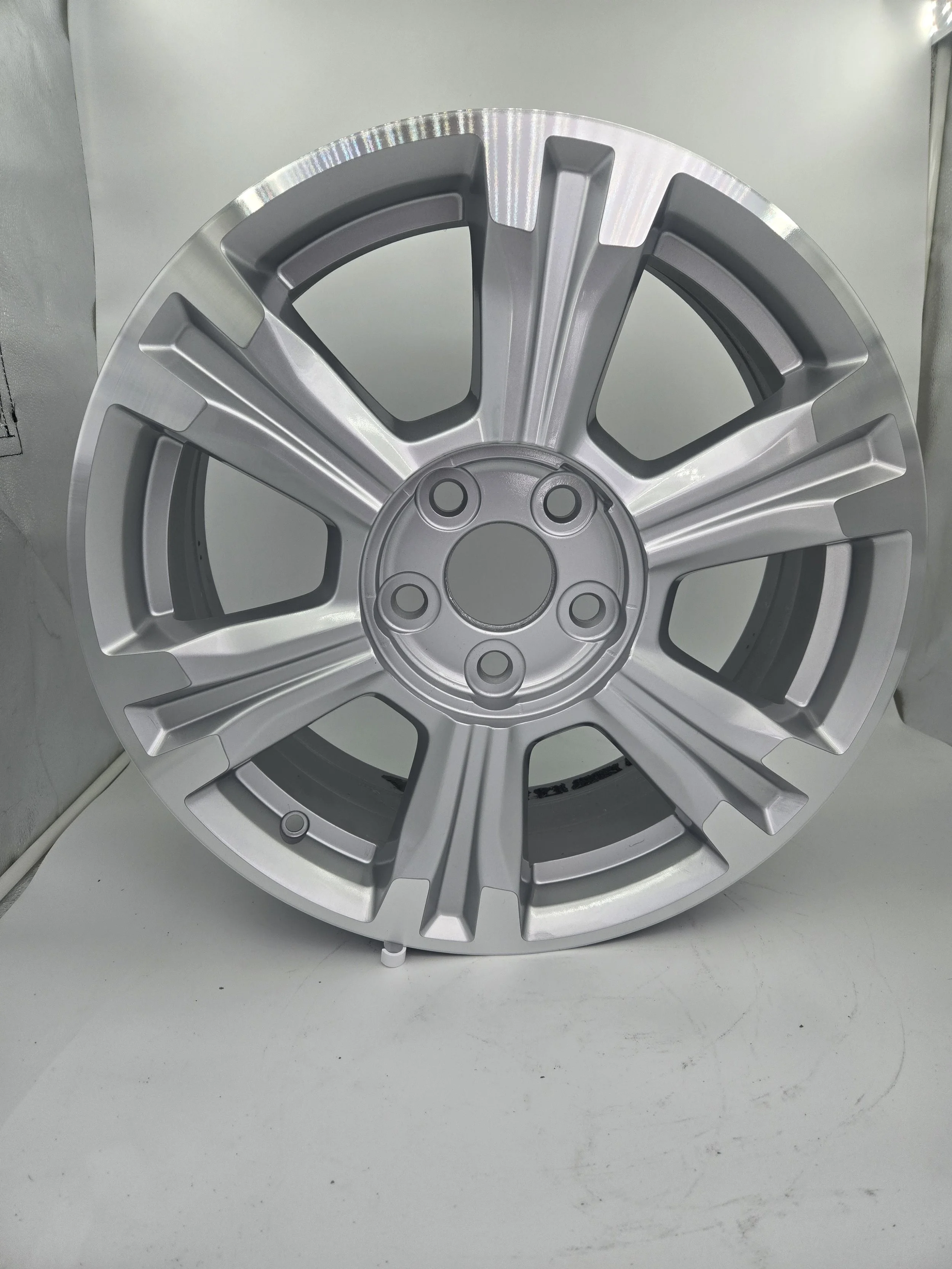 A silver alloy car wheel rim with a five-spoke design, placed on a white surface.