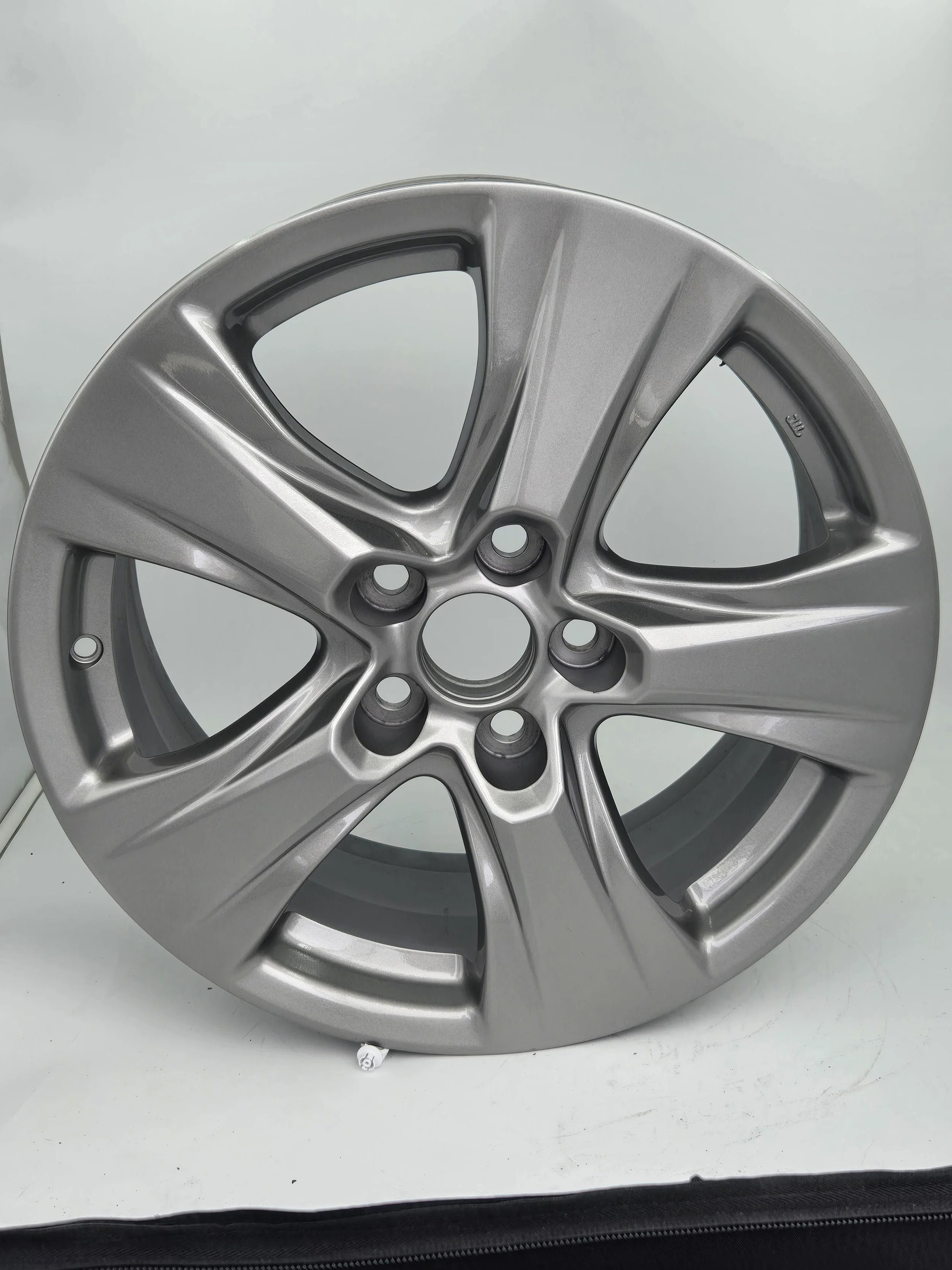 A silver alloy car wheel rim on a white surface with a plain light blue background.