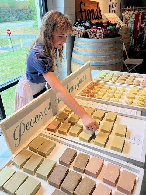A young girl shopping for soap bars at a store, standing by a display of various soap varieties.