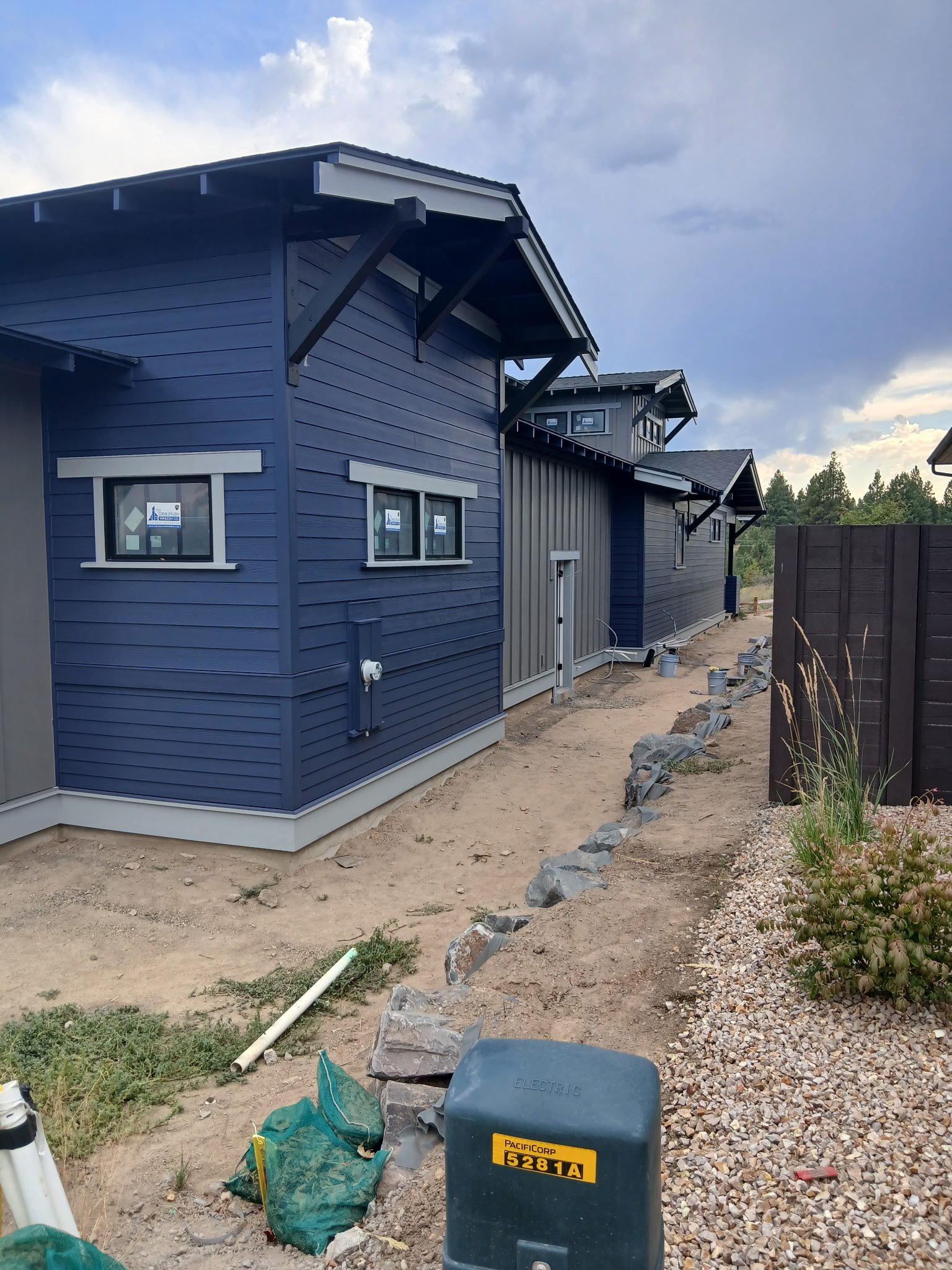 Construction site at a row of newly painted blue and gray houses with some construction materials and tools on the ground.