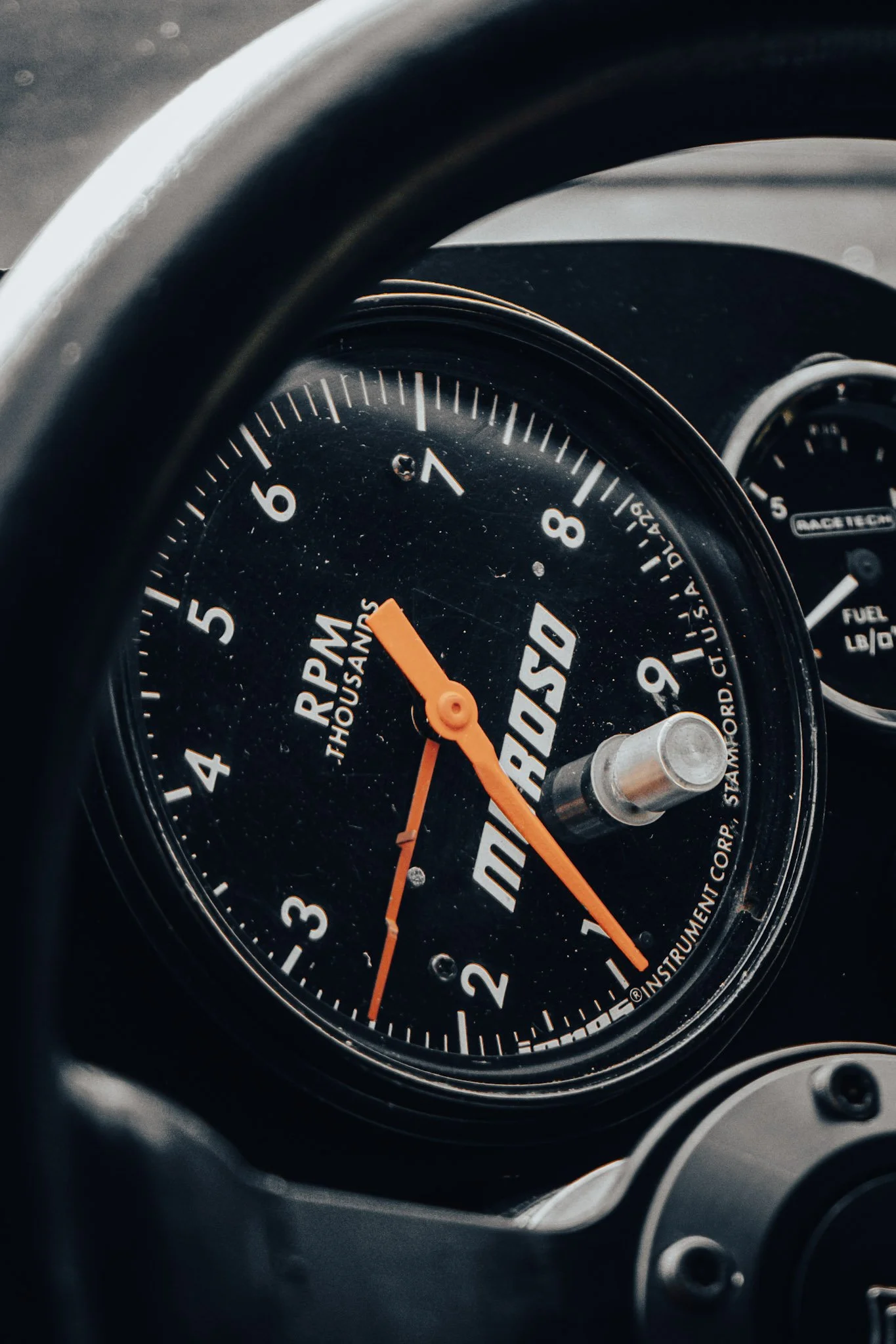 Close-up of a car dashboard gauge showing the tachometer with the needle pointing around 1,000 RPM, and the speedometer in the background.