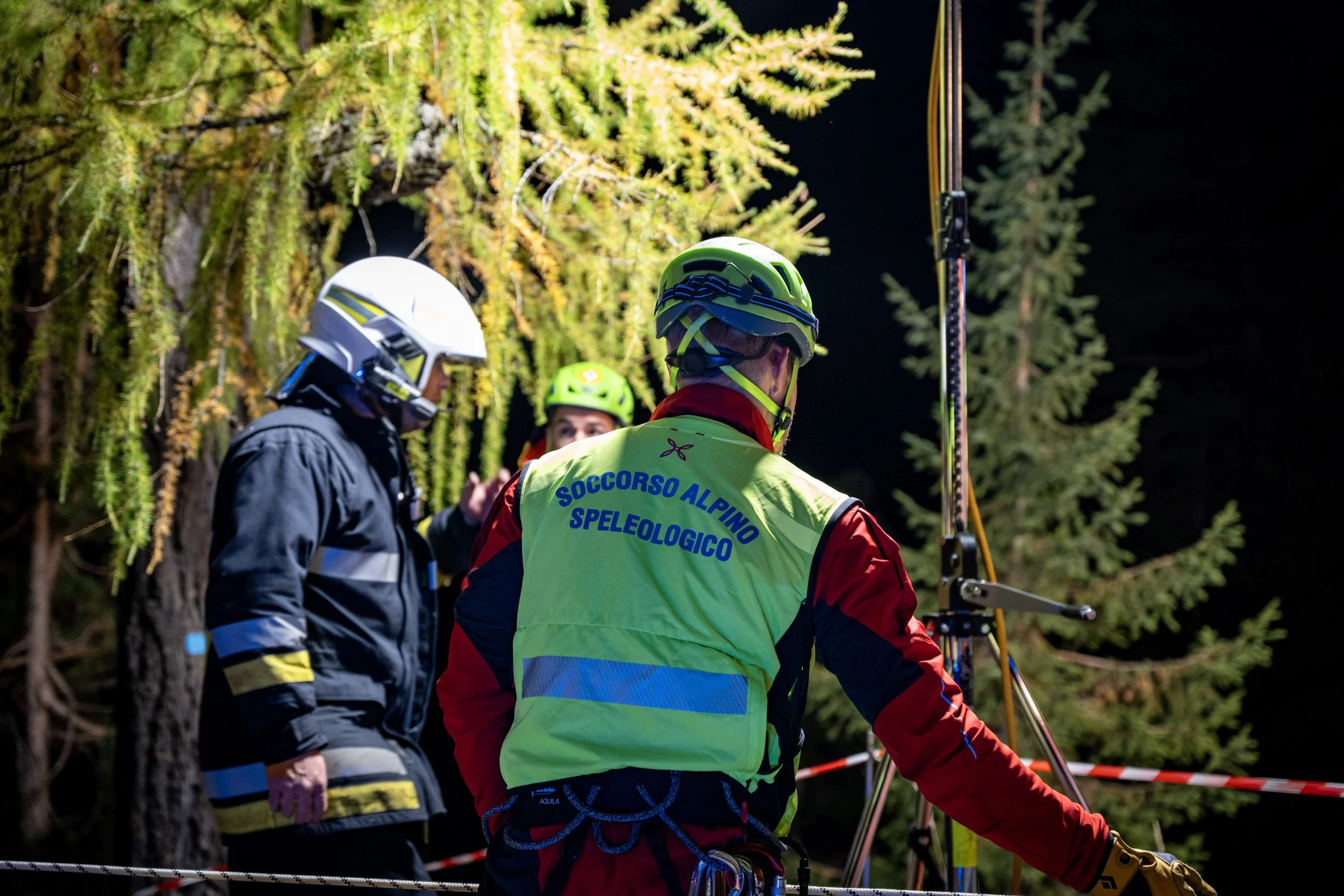 Group of rescuers in helmets and safety gear conducting a night-time rescue operation in a forested area.