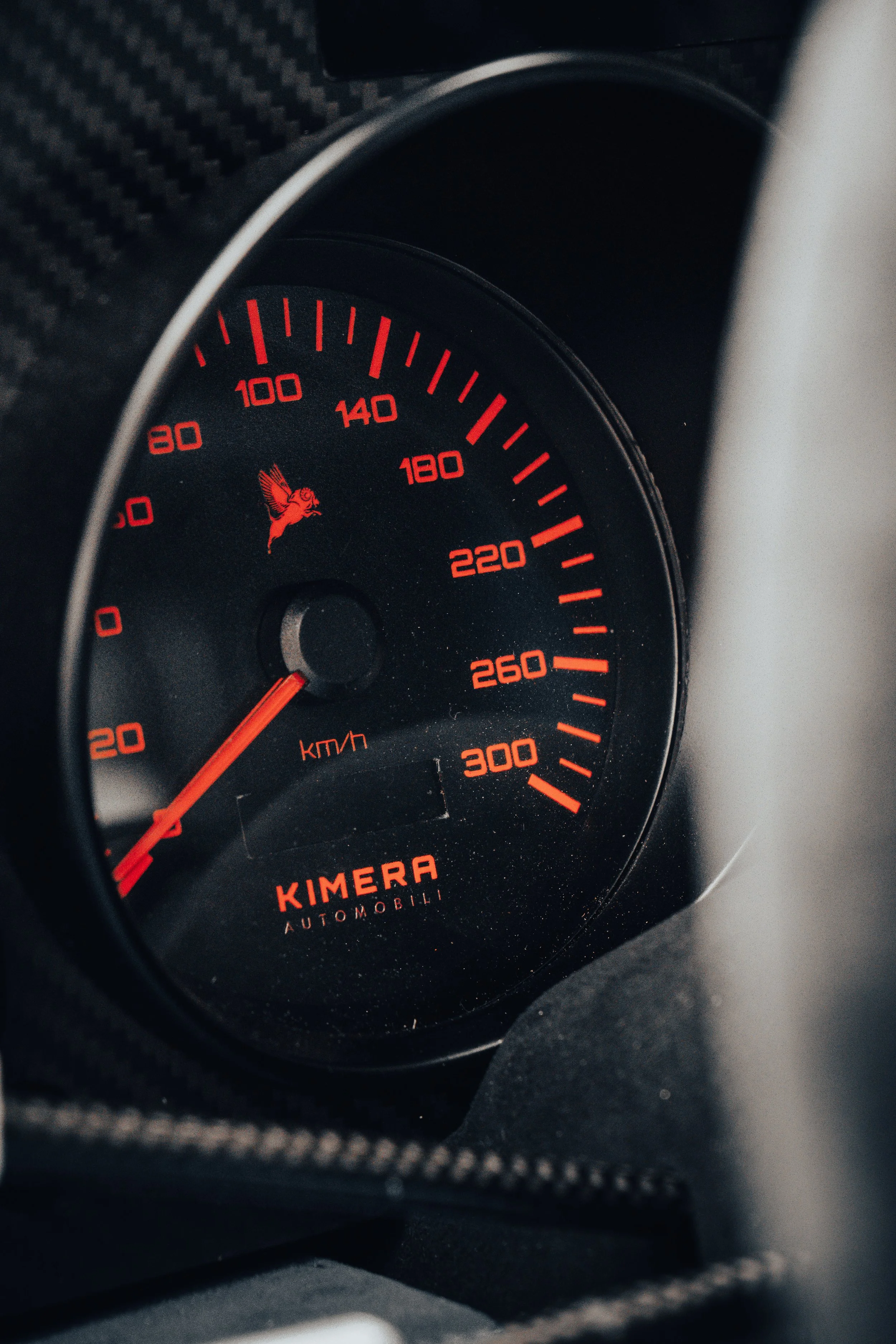 Close-up of a car speedometer with a red bird logo, showing a speed of approximately 60 km/h, with the brand name 'KIMERA AUTOMOBILI' in red.