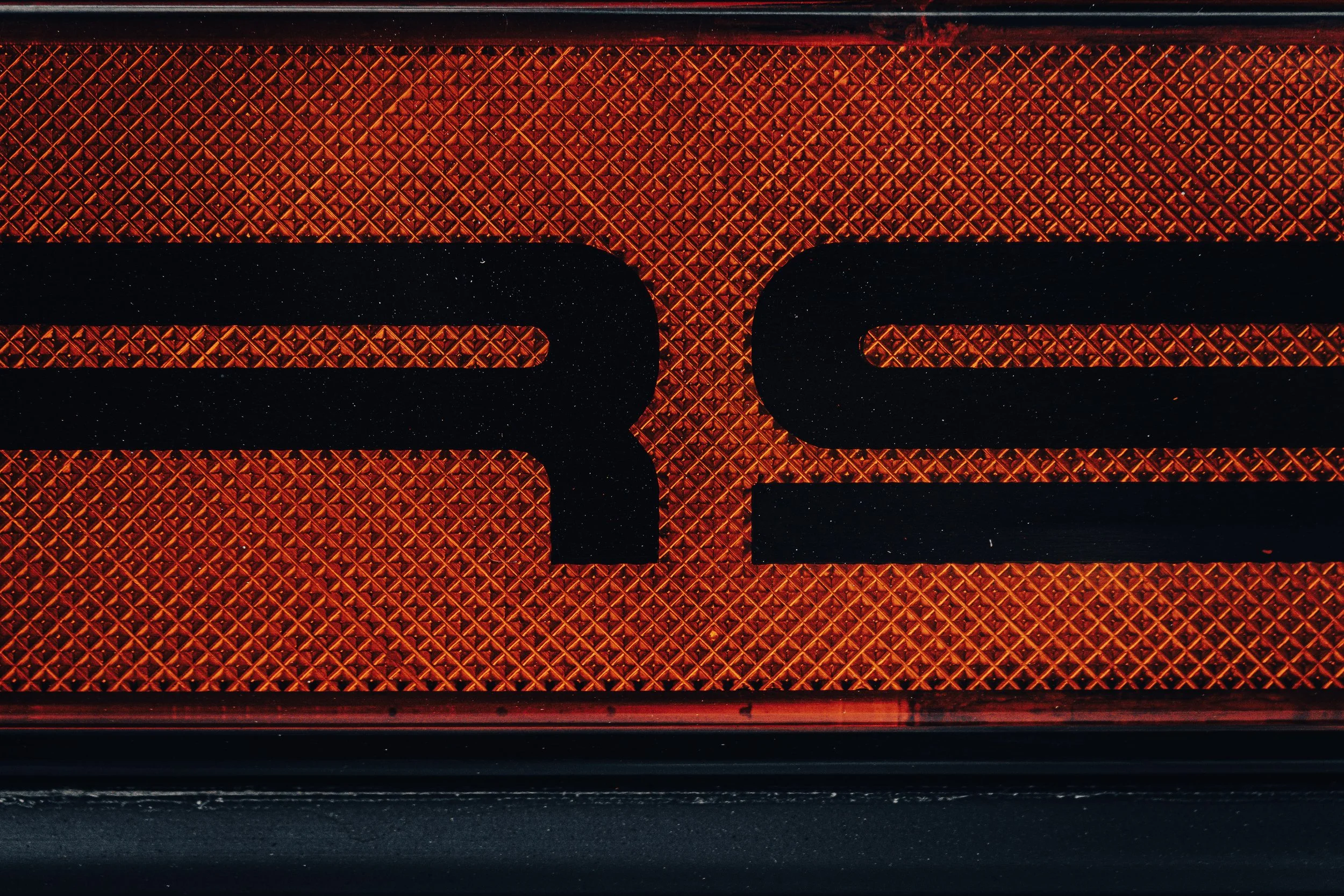 Close-up of a red reflective traffic signal or indicator with a textured diamond pattern, showing part of a black symbol or letter.