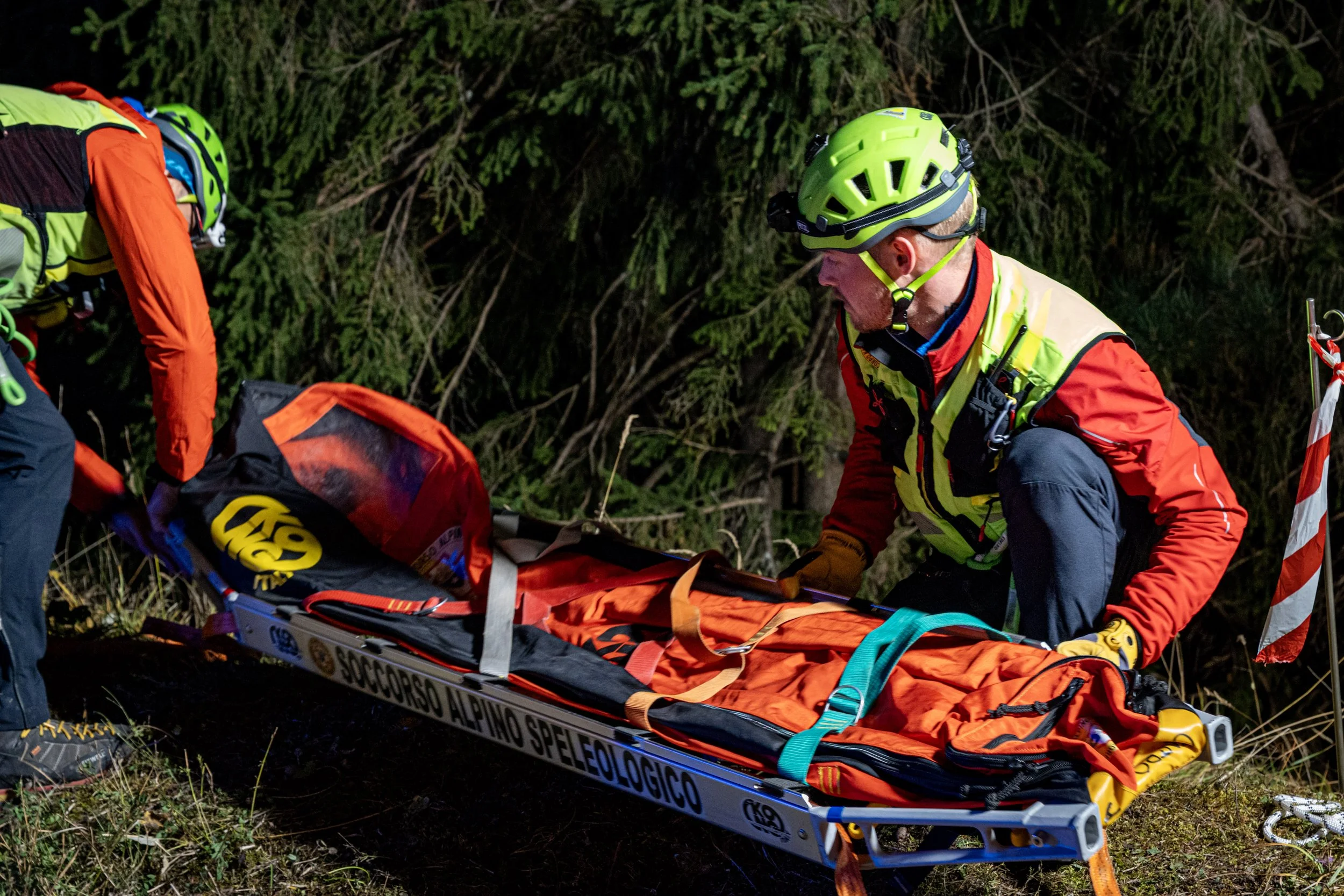 Emergency rescue workers in bright safety gear preparing a stretcher in a forested area at night.