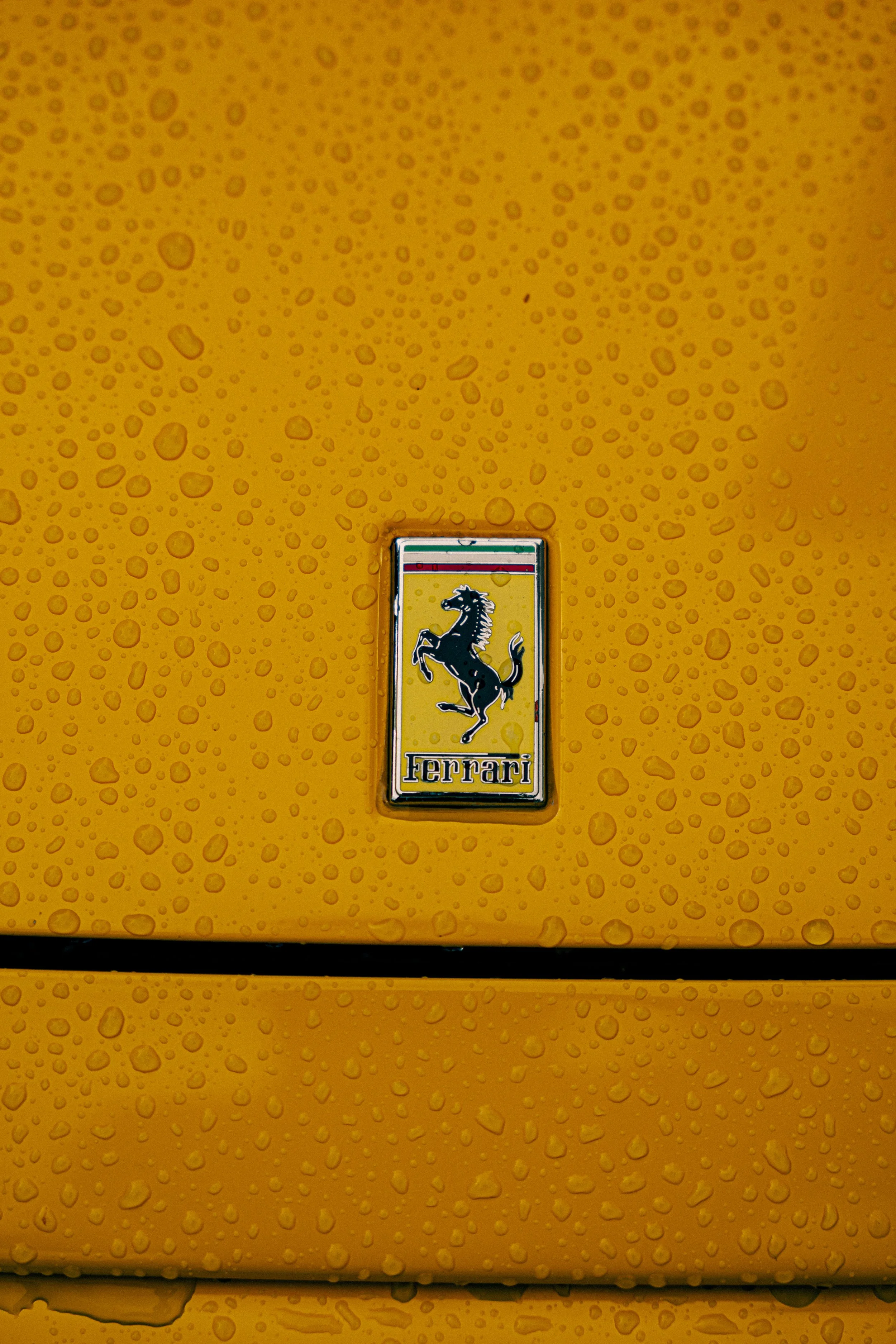 Yellow Ferrari car with water droplets on its surface and a Ferrari badge in the center of the image.