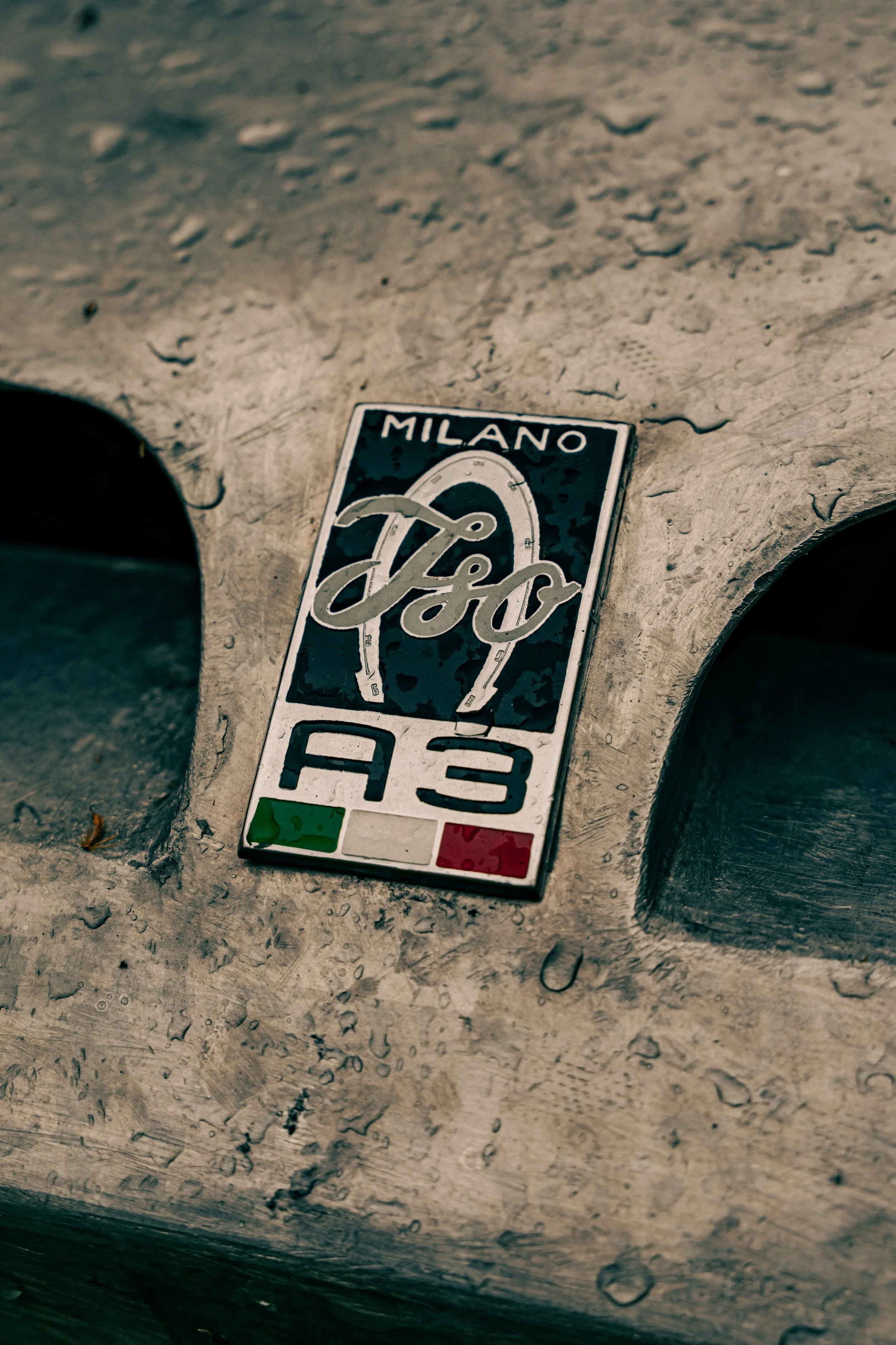 Close-up of a plaque on a brick wall with the Italian flag colors and the word 'Milano' at the top. The plaque features a horseshoe shape with the words 'A3' underneath, possibly indicating a highway exit or route near Milan, Italy.