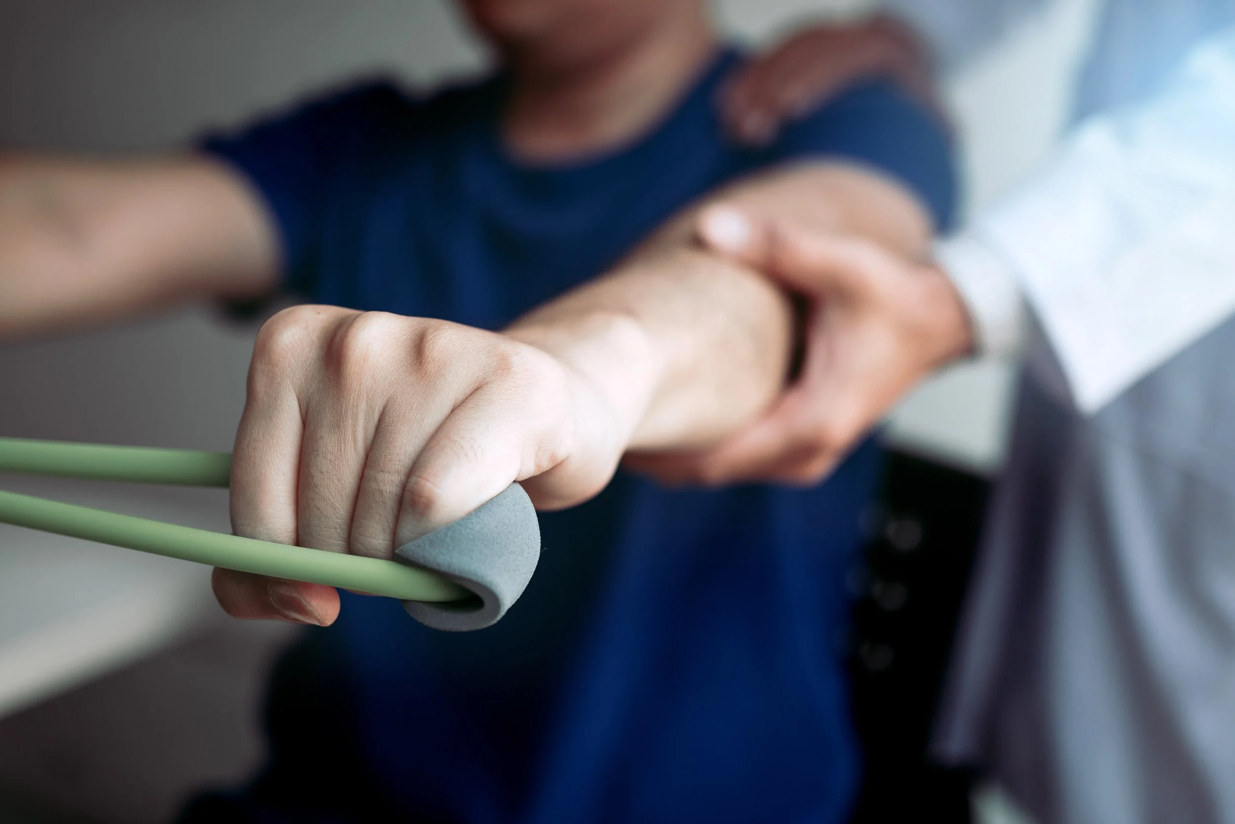 Close-up of a person's hand gripping a gymnastic or climbing hold, with another person's hand resting on their shoulder in the background.