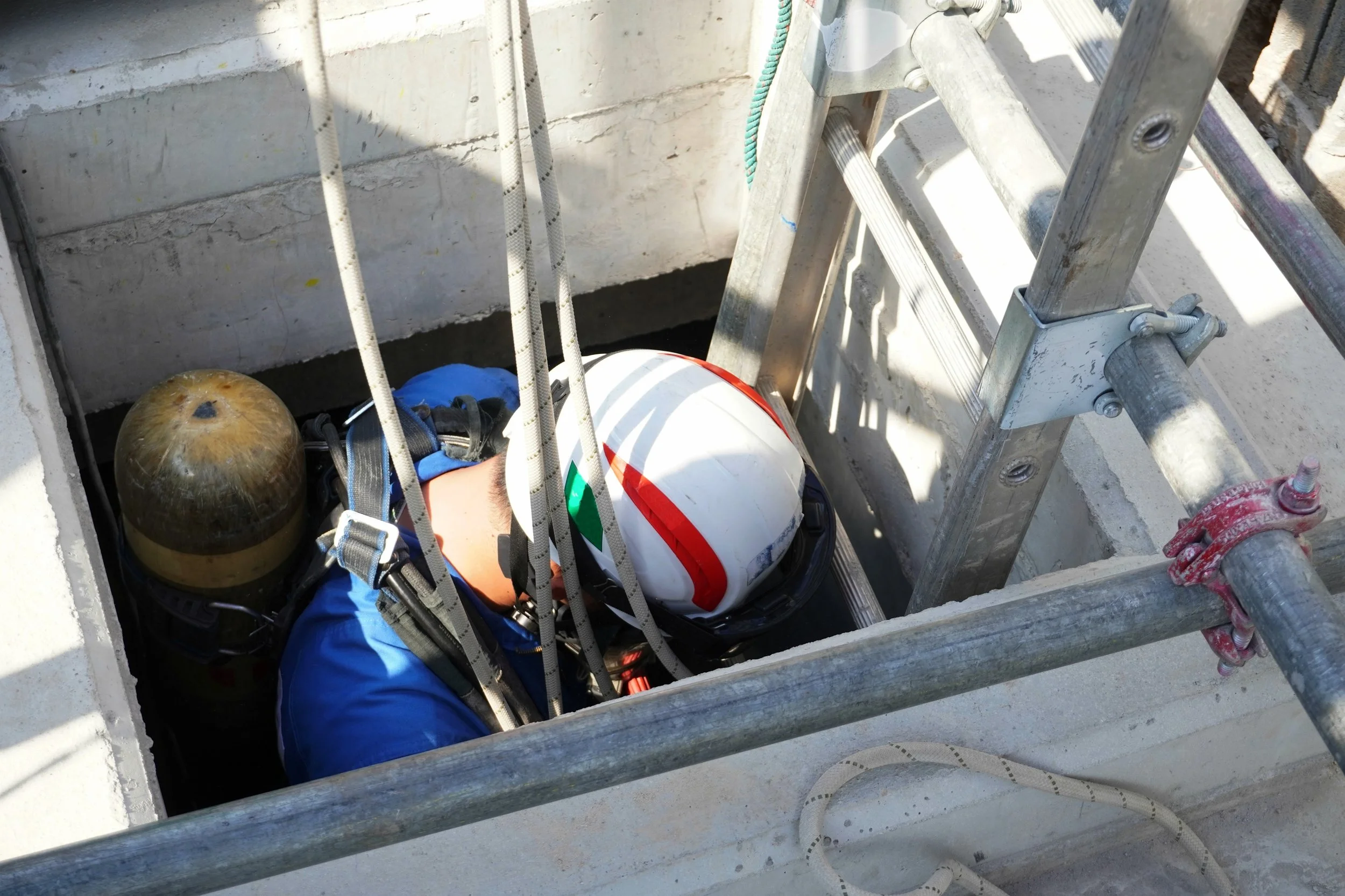 Industrial worker accessing a confined construction space using safety equipment and fall protection.