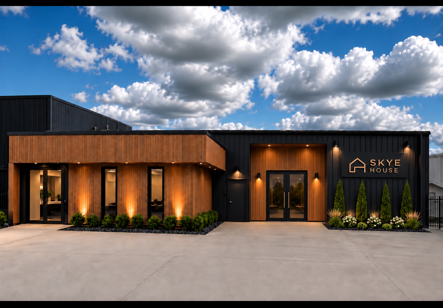 Modern commercial building with black and wood exterior, illuminated landscaping, and sign reading 'Skye House' under a partly cloudy sky.