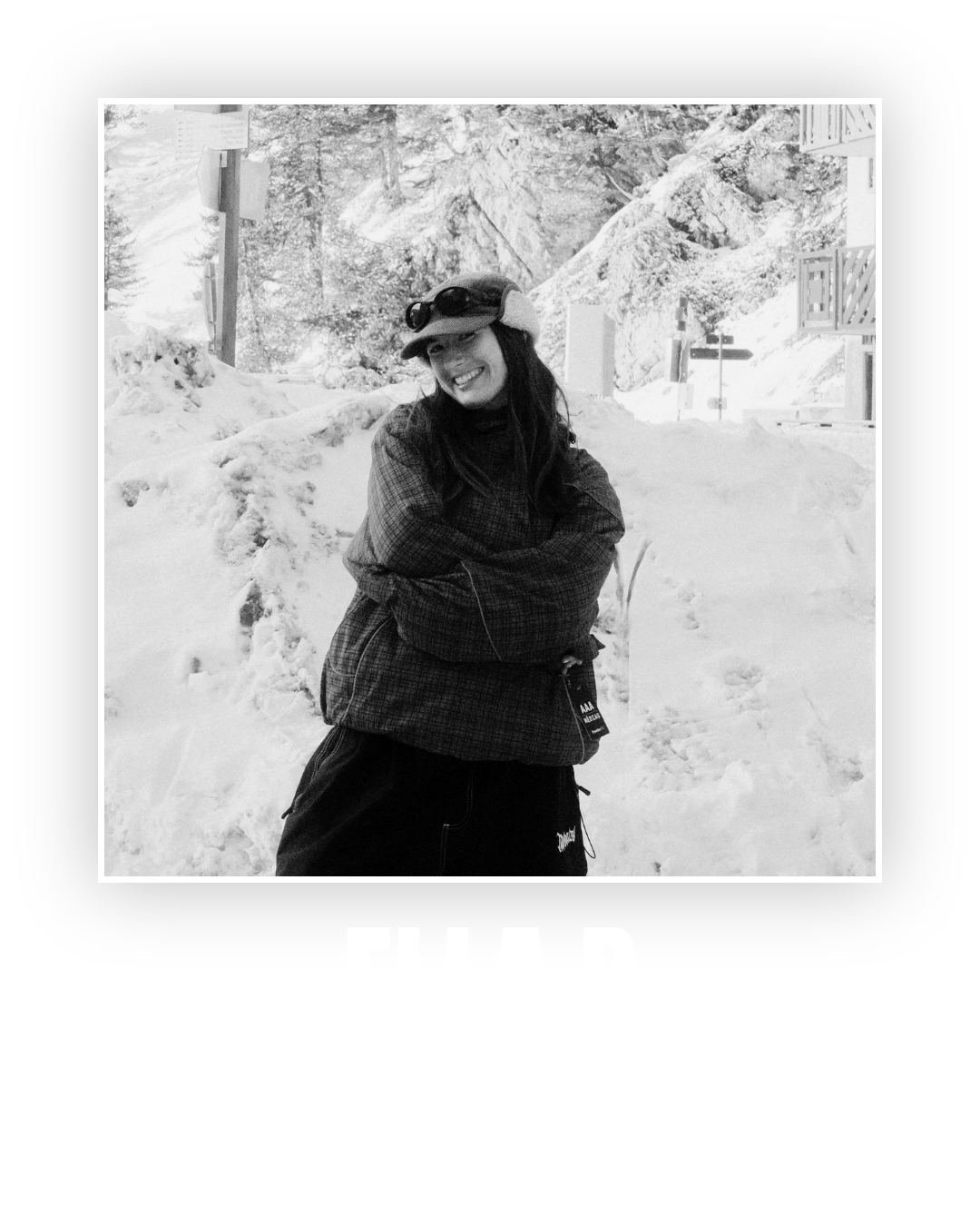 A woman smiling in a snowy outdoor setting, wearing a cap and winter clothing.