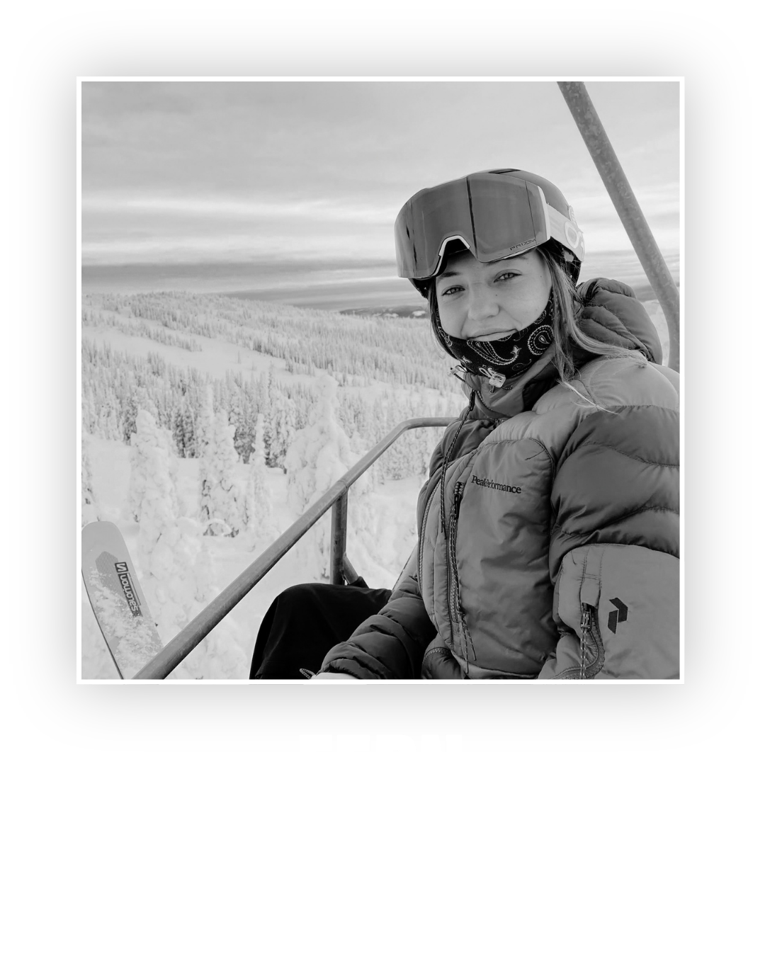 A woman in winter sports gear, wearing a helmet and a face mask, sitting on a ski lift with snow-covered trees and a cloudy sky in the background.