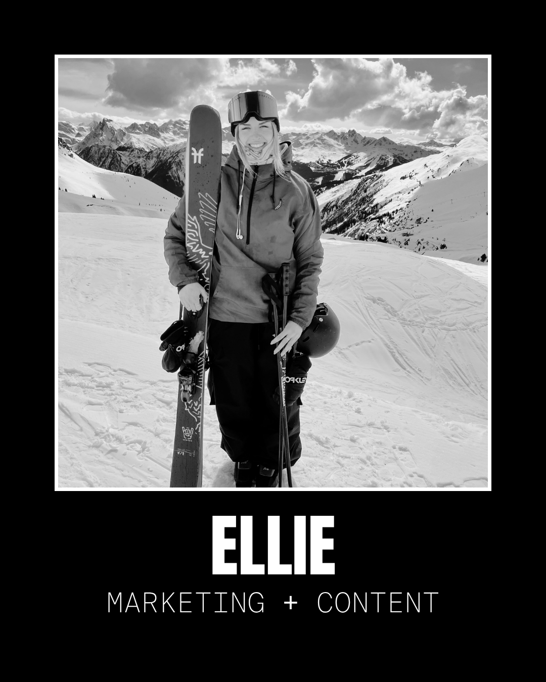 A woman in winter gear holding skis and a helmet, standing on snow-covered mountains with a scenic backdrop of mountains and clouds.