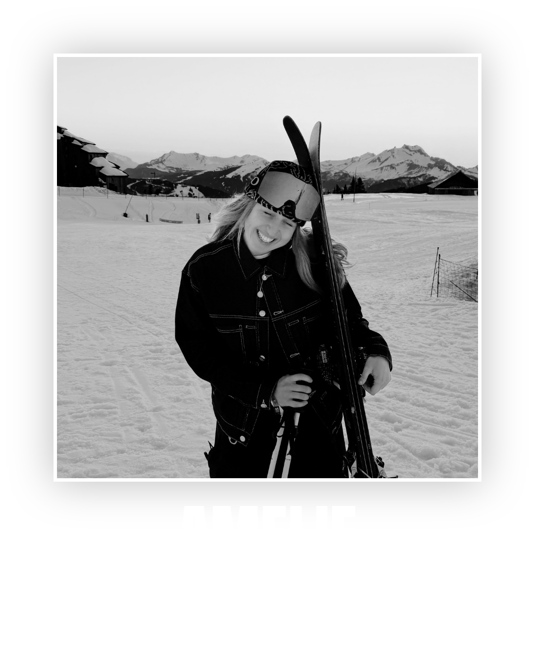 A woman in ski gear holding skis on a snowy mountain landscape in black and white.