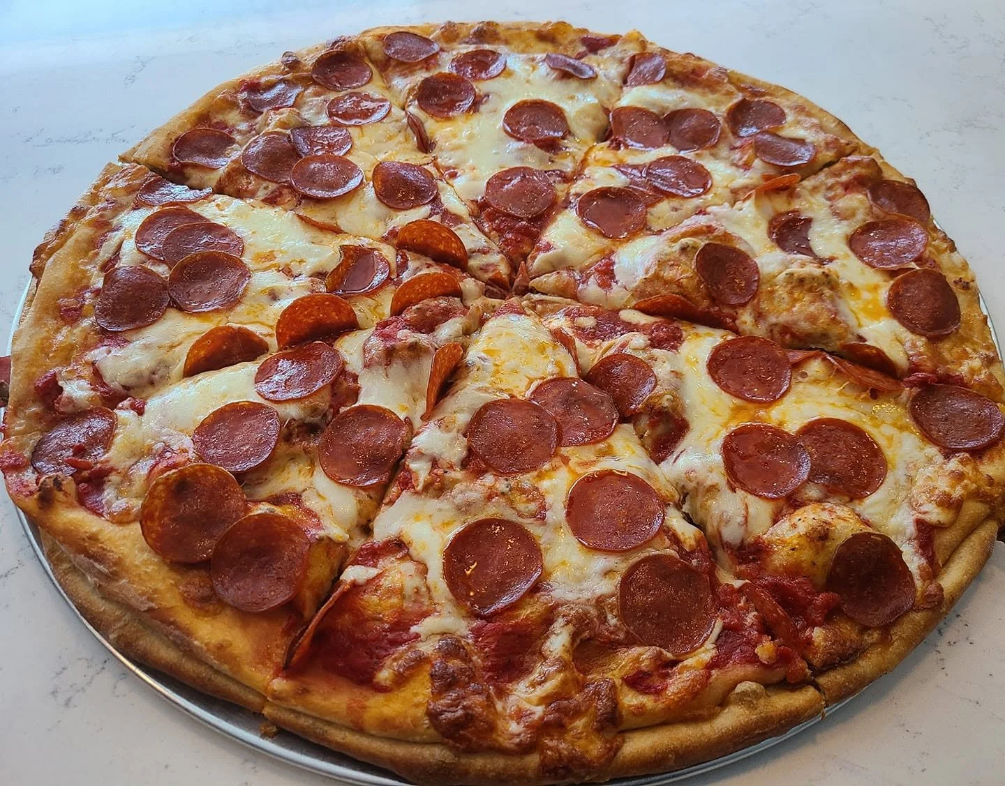 A pepperoni pizza with visible cheese and pepperoni slices on a round metal tray.