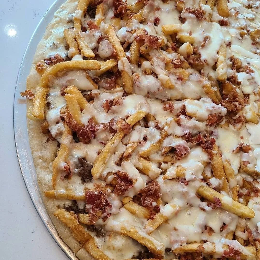 Close-up of a pizza with cheese, bacon, and French fries on top.