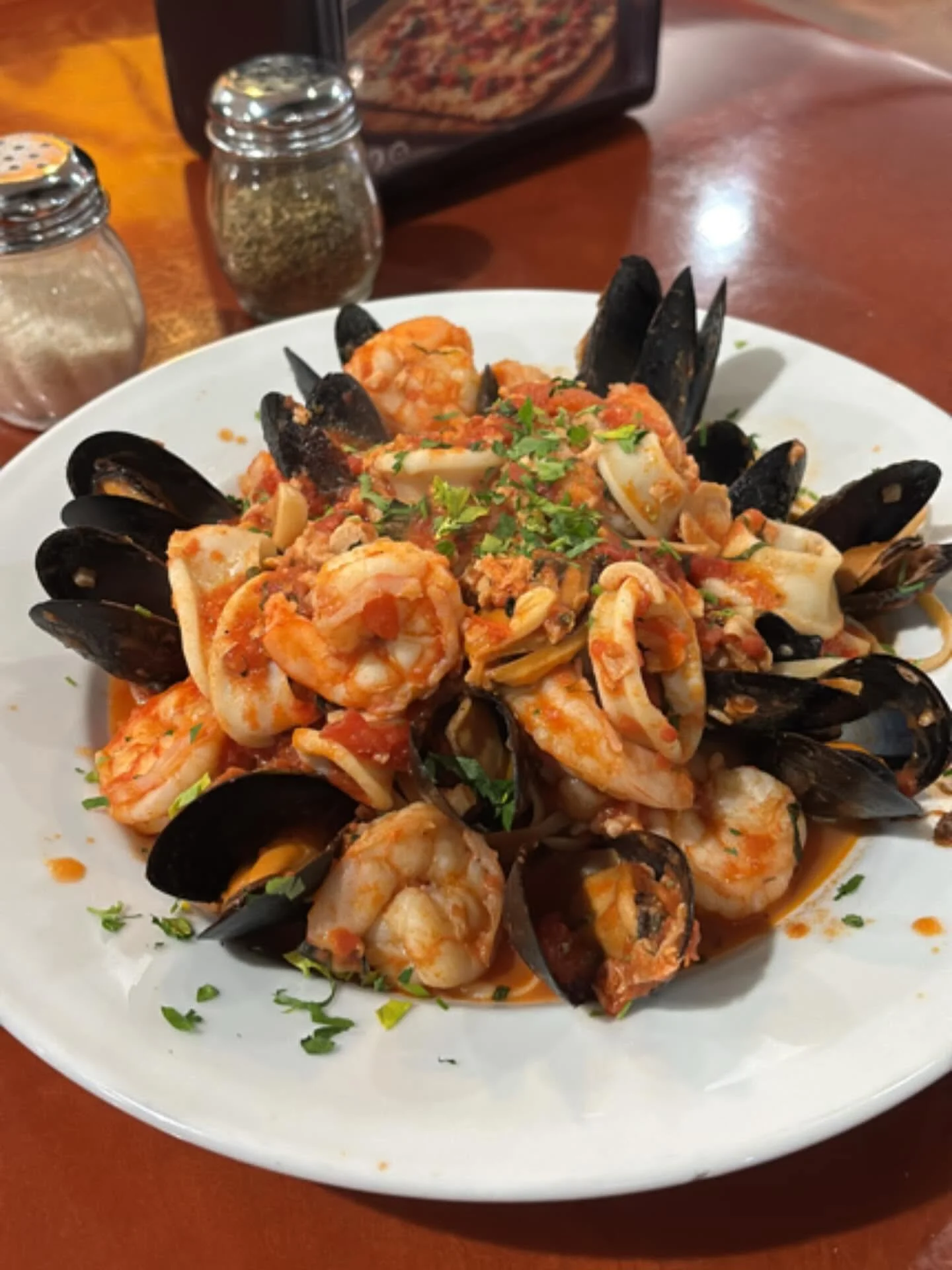 A plate of seafood pasta with shrimp, mussels, and squid garnished with chopped parsley.