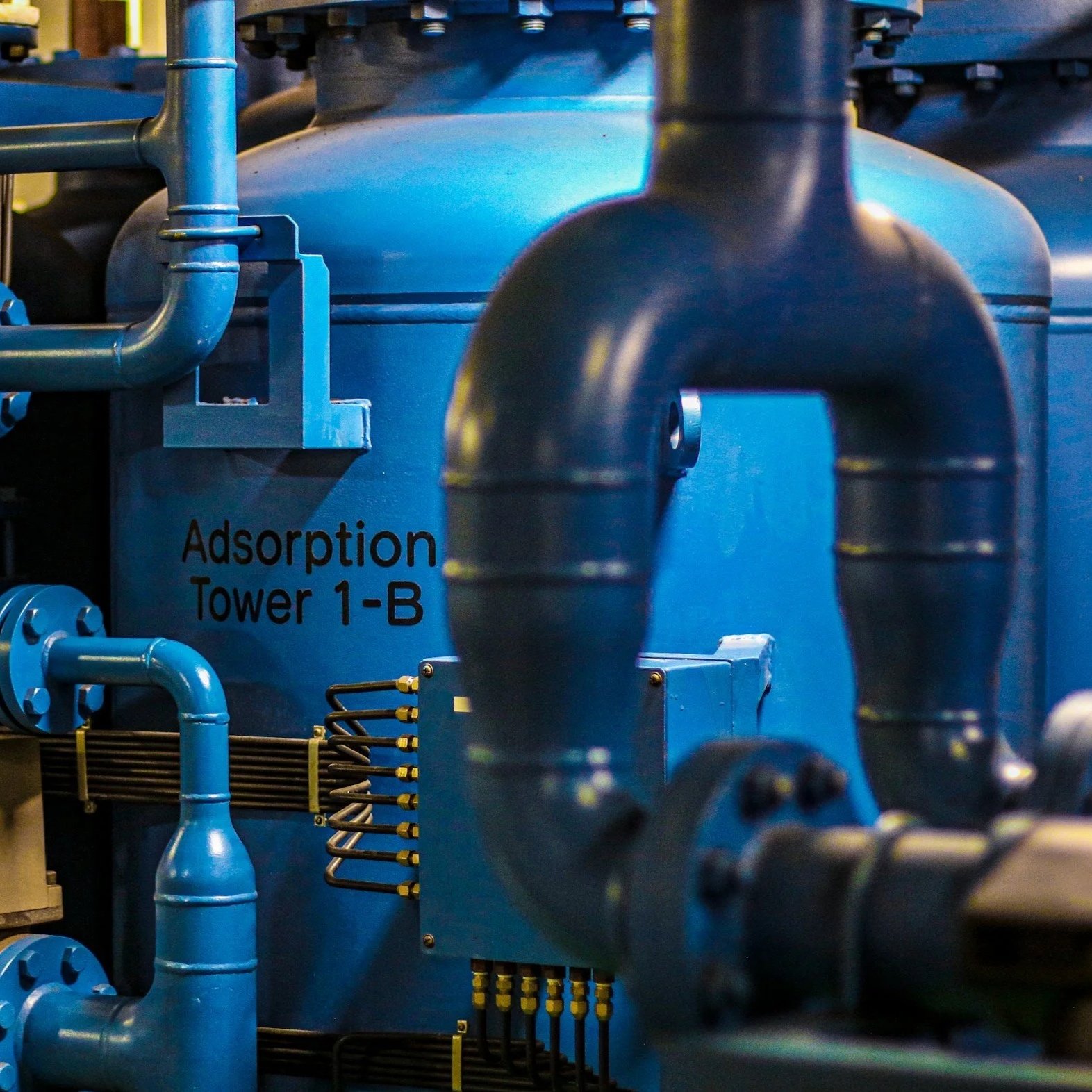 Close-up of a large industrial machine with blue pipes and components, labeled "Adsorption Tower 1-B".