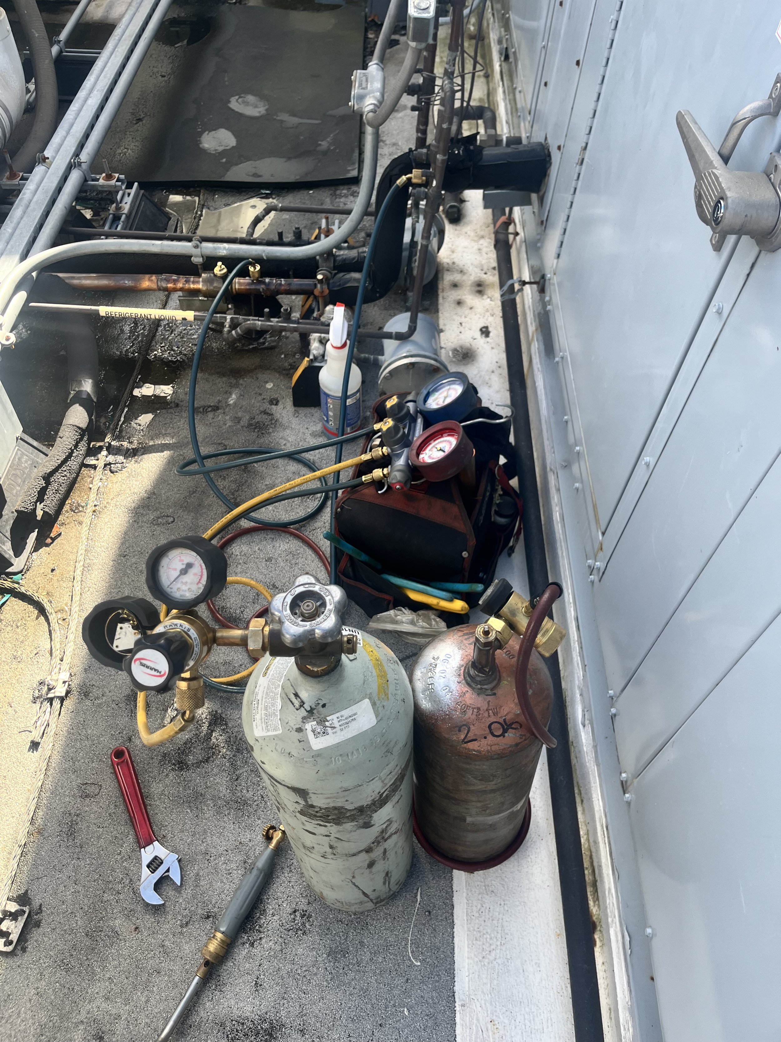 HVAC service area with refrigerant tanks, gauges, and tubing.