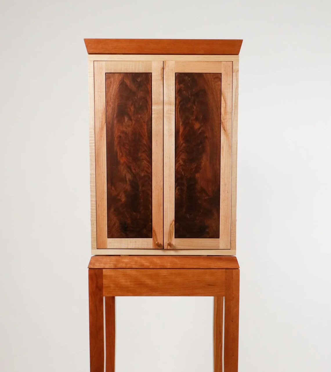 A wooden display cabinet with two doors, sitting on a matching wooden stand, against a plain white background.