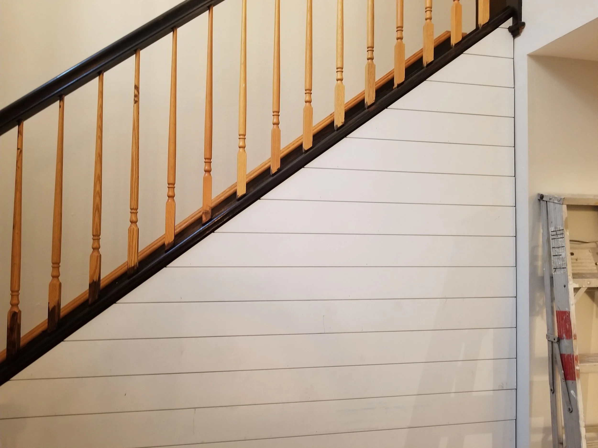 Interior attic with staircase, a ladder, and white wall panels.